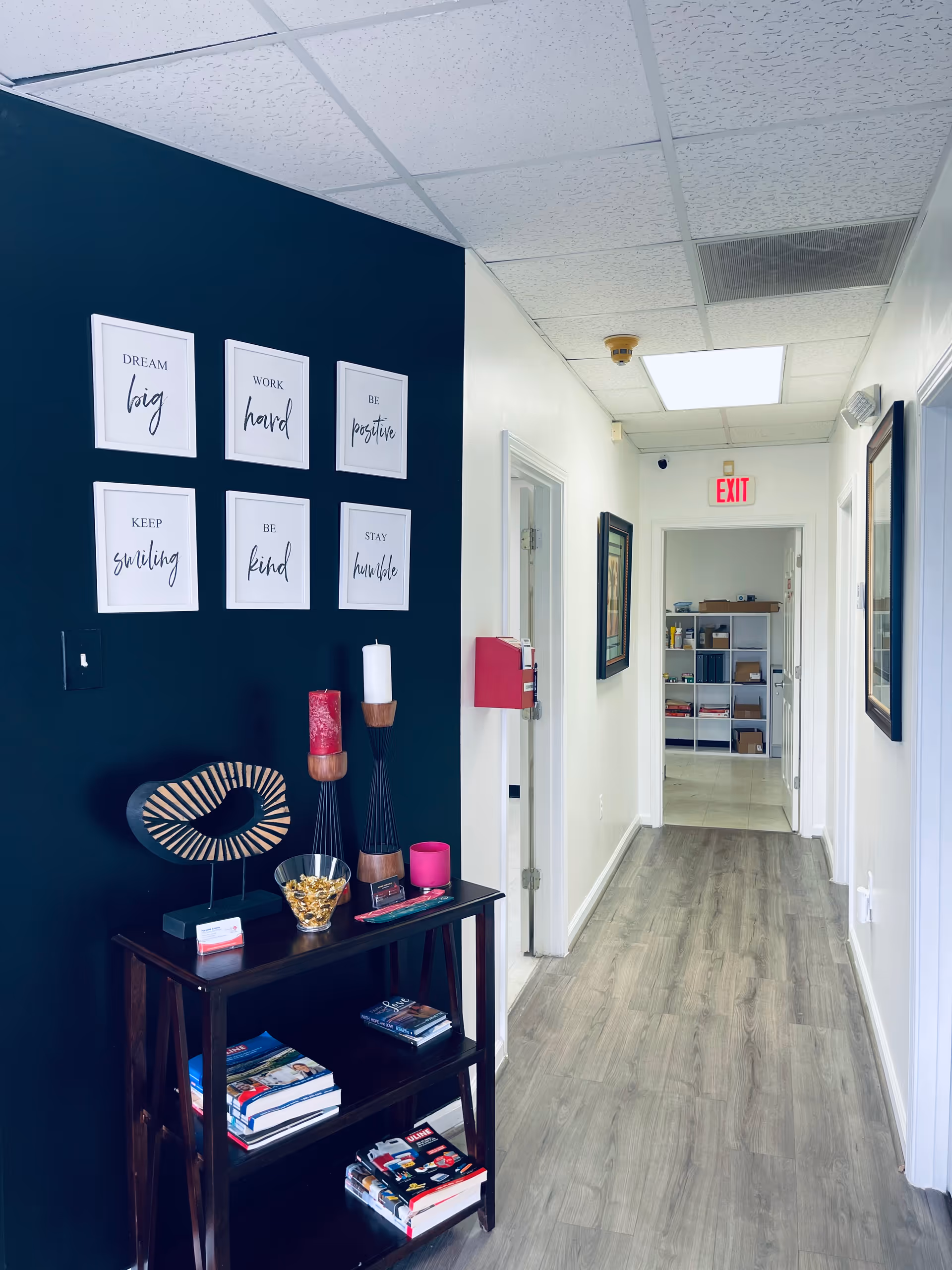 Narrow hallway with dark blue accent wall, framed quotes, and a small console table.