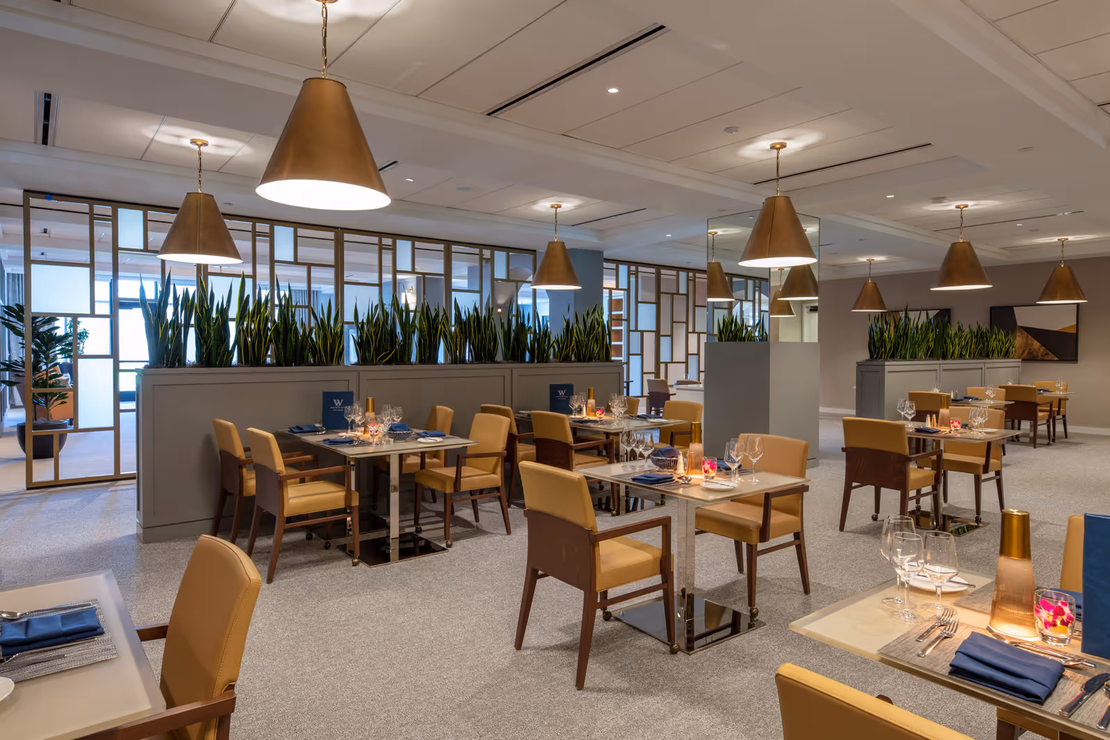 Modern senior dining room with neatly arranged tables and chairs, pendant lights, and planters dividing the space.