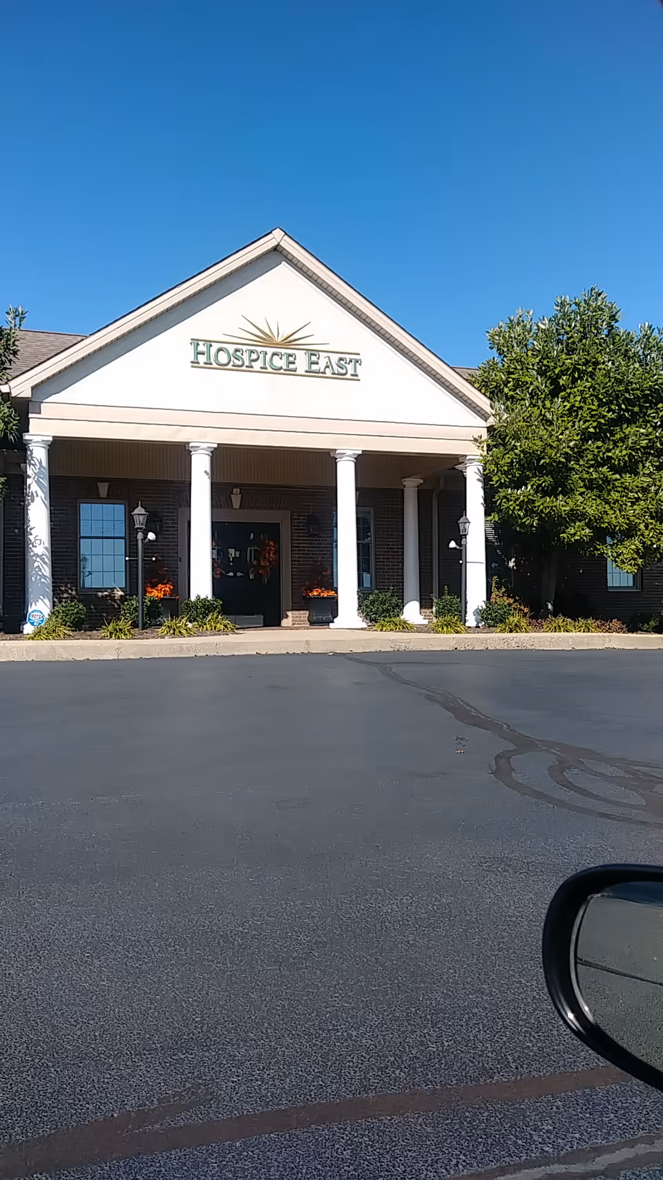 Front view of Hospice East building with a covered entrance and columns, parking lot in foreground.