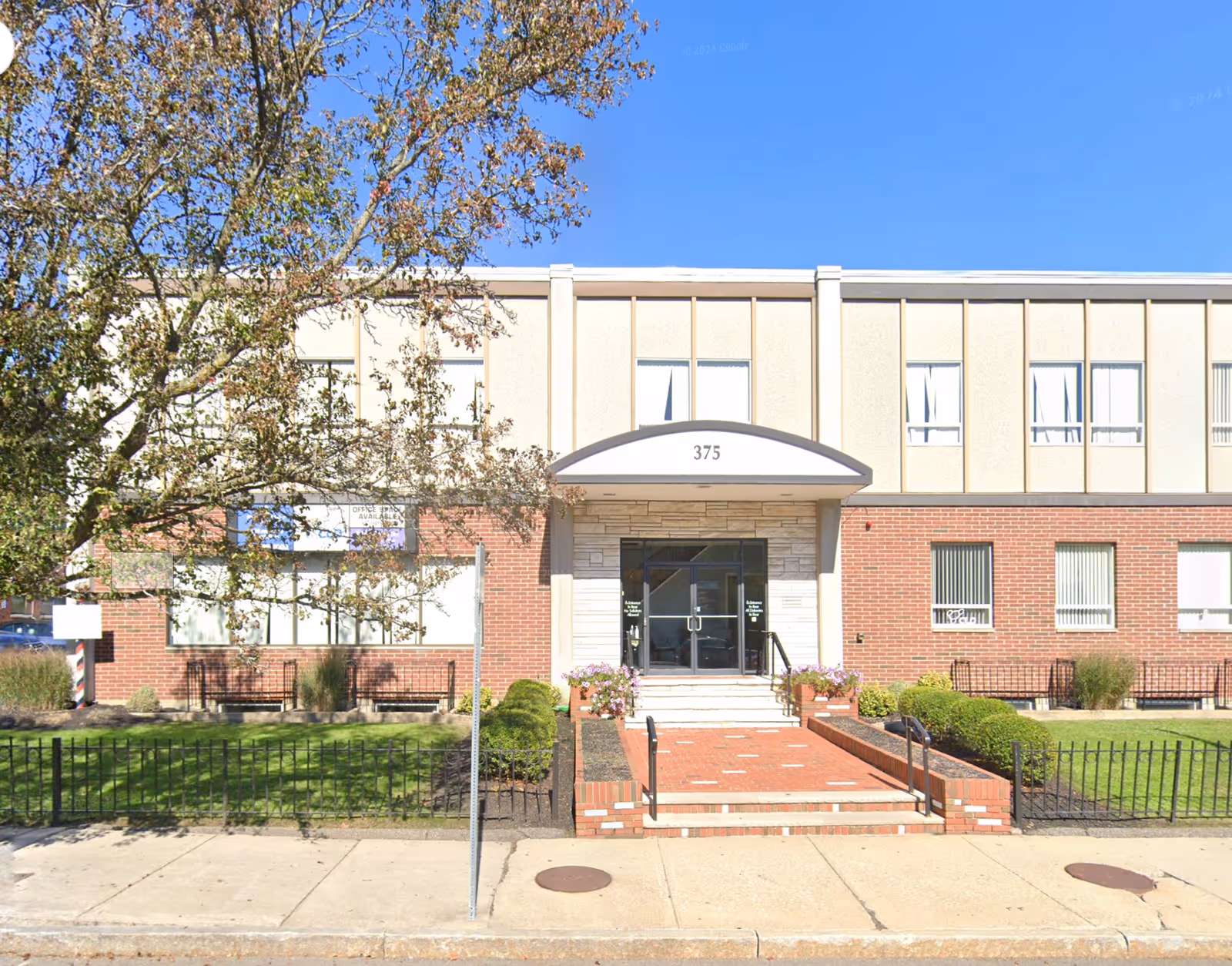 Front view of an entrance with curved canopy, glass doors, and brick beige facade.