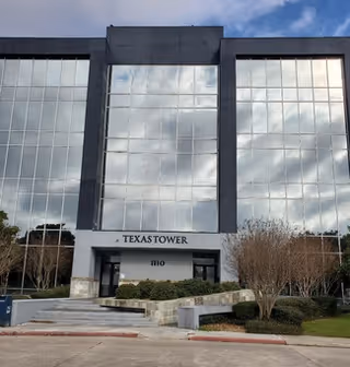 A modern glass-front building with a centered entrance labeled TEXASTOWER and landscaping.