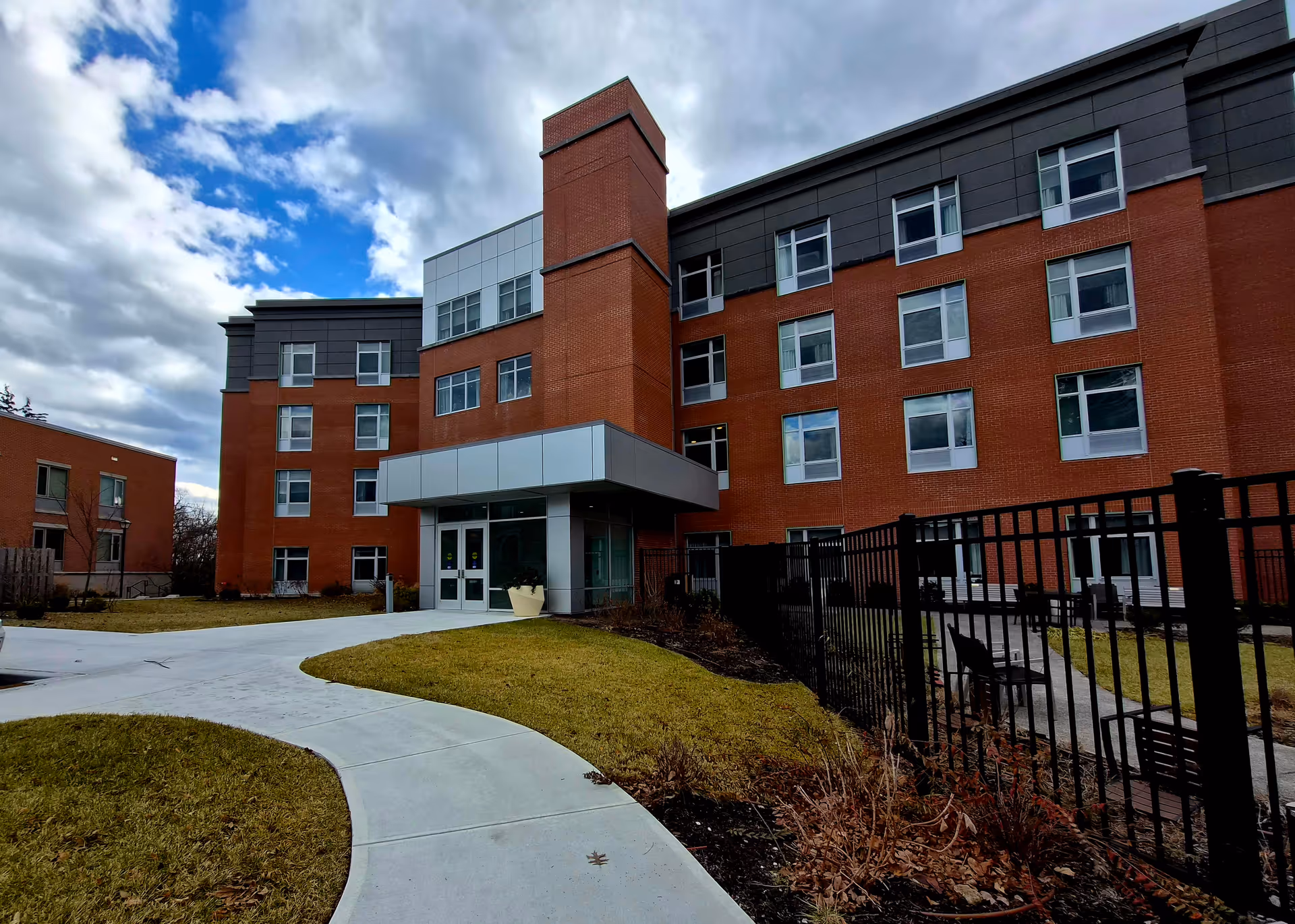 Red brick Wartburg Home senior living building with curved walkway and fenced outdoor seating.