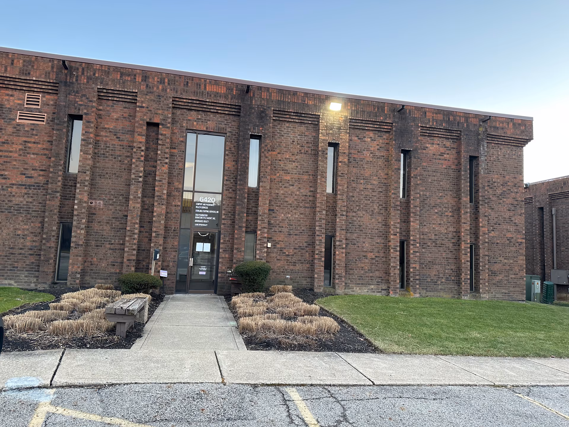 Brick facility exterior with glass entrance, walkway, and landscaped shrubs