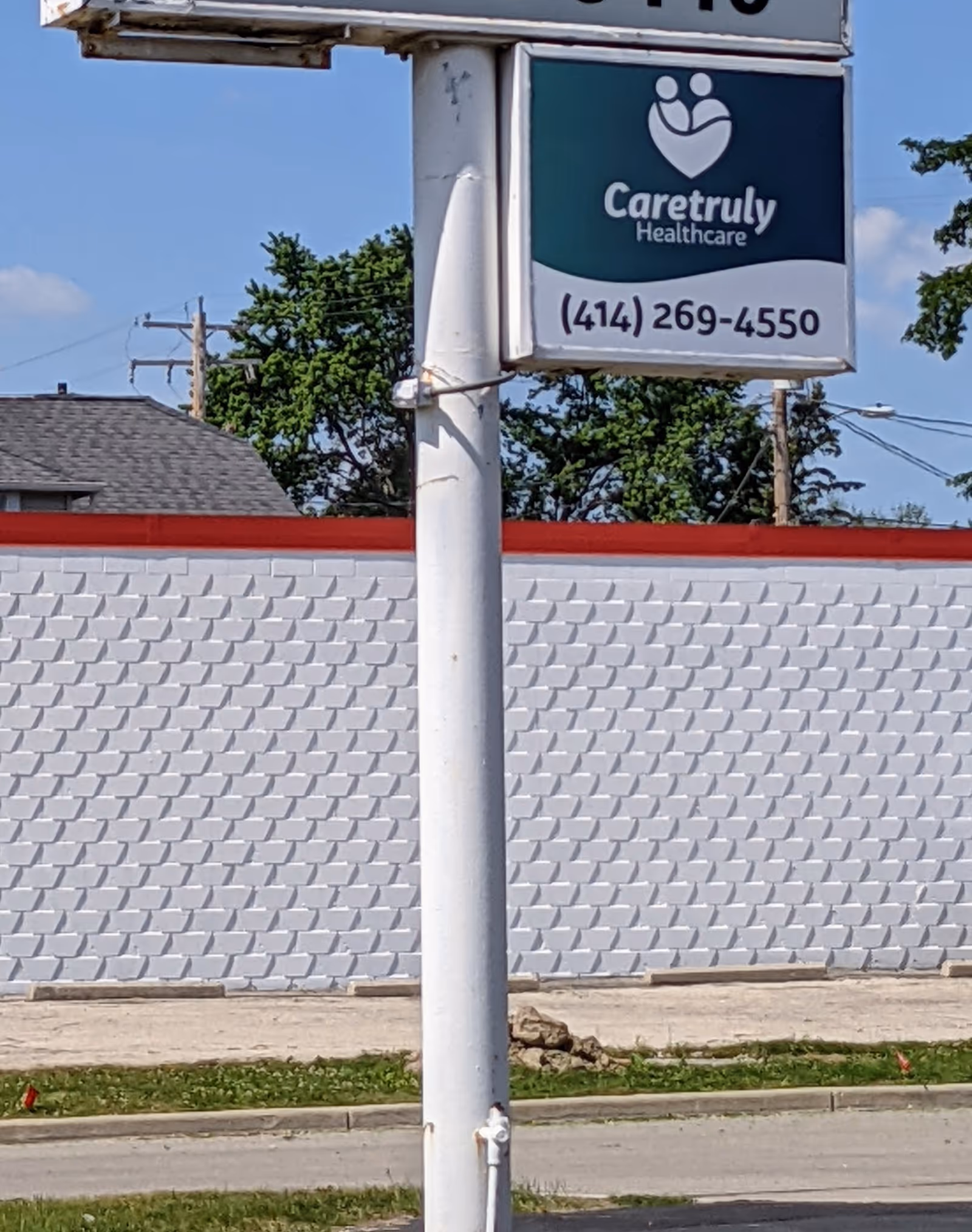 Outdoor scene with CareTruly Healthcare sign mounted on a pole in front of a patterned wall