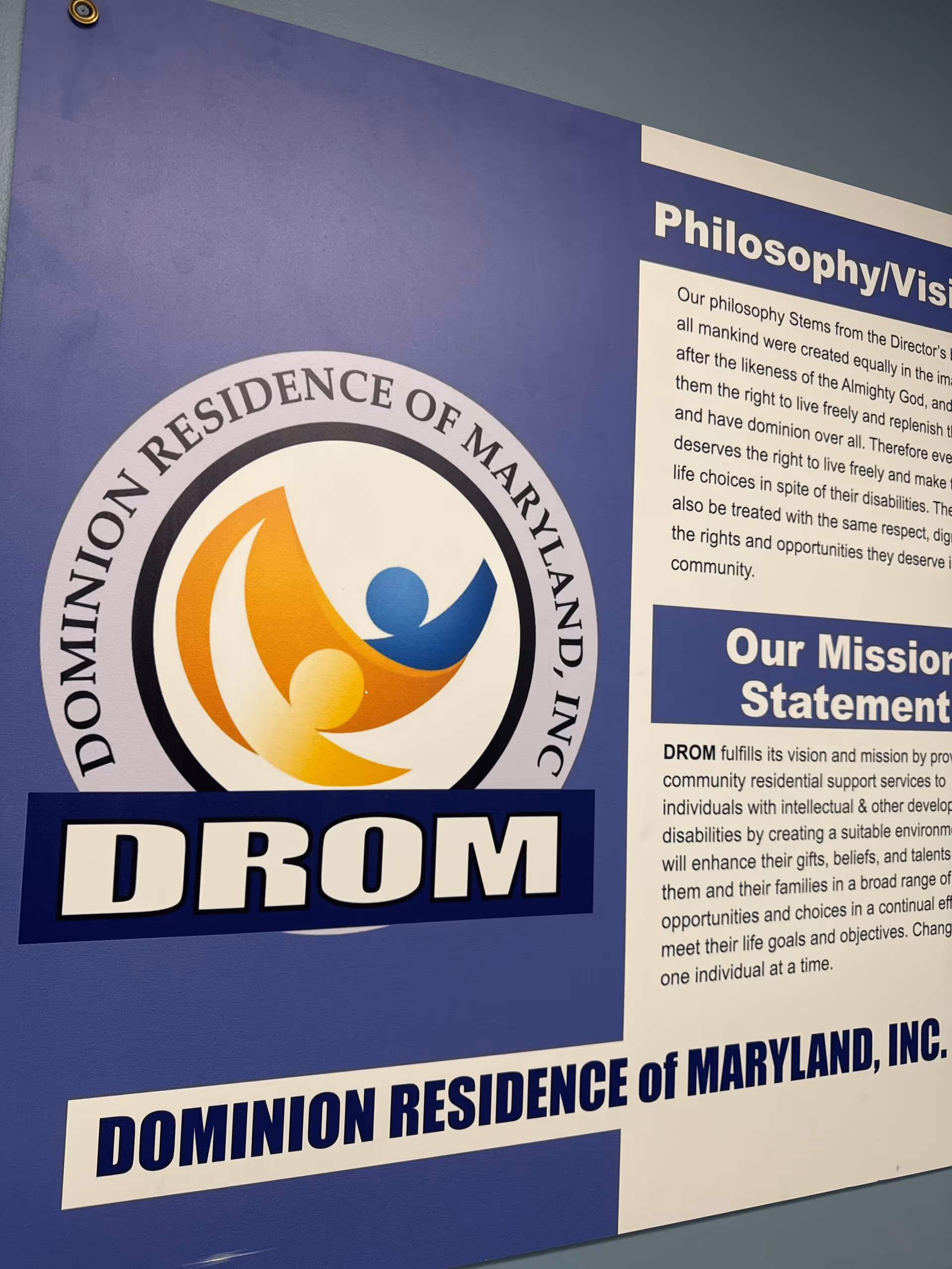 Blue wall sign displaying Dominion Residence of Maryland logo and mission text.