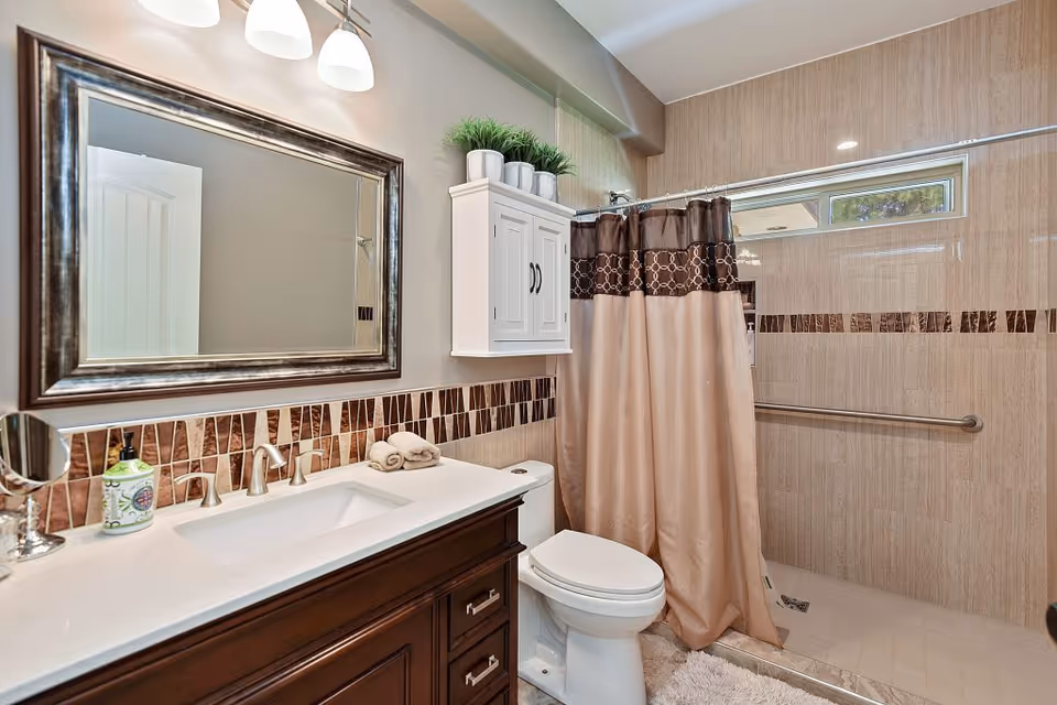 Modern bathroom with double sink vanity, toilet, framed mirror, and tiled shower.