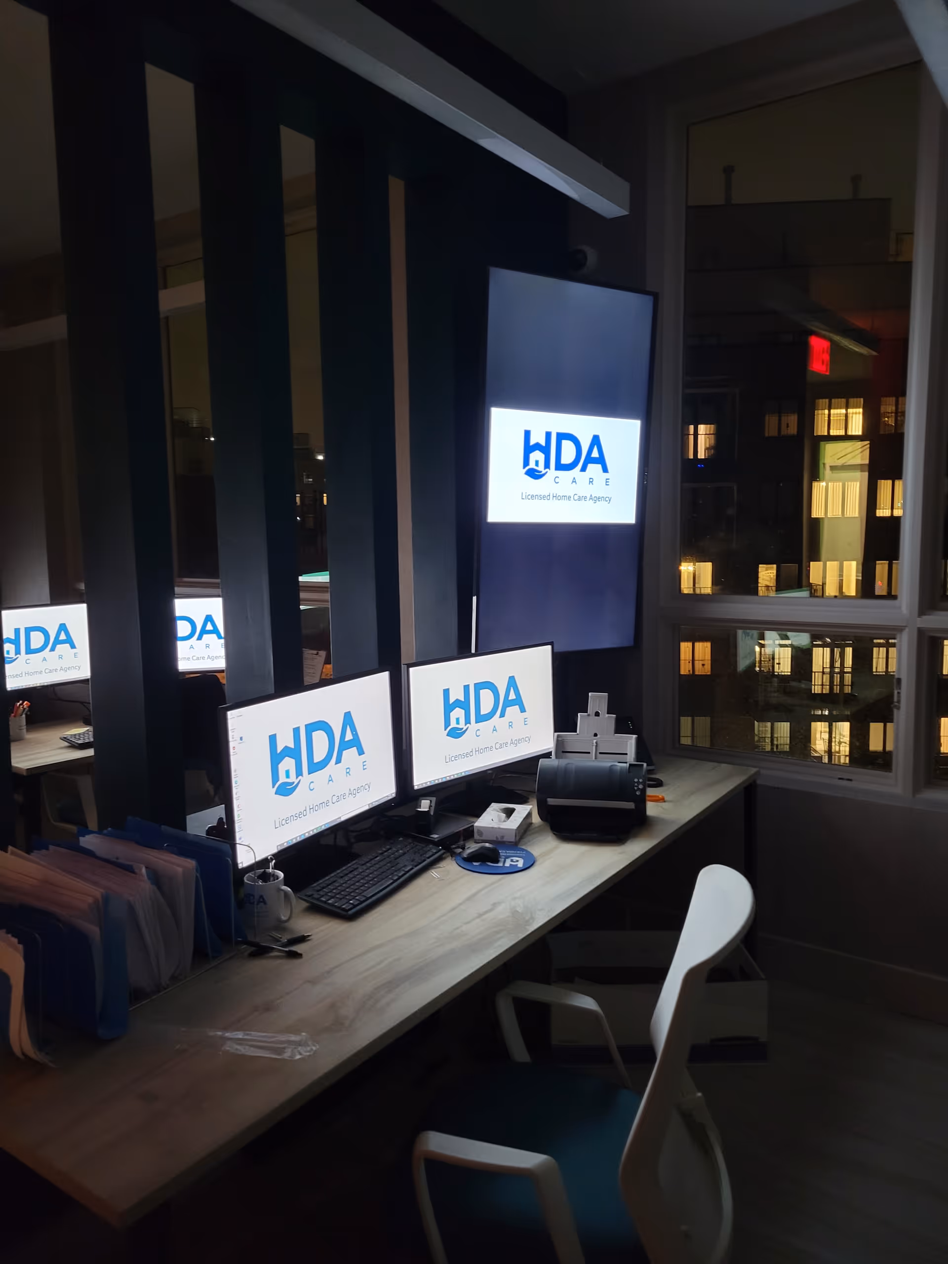Office workspace inside a senior care facility with multiple computer monitors displaying HDA CARE logos.