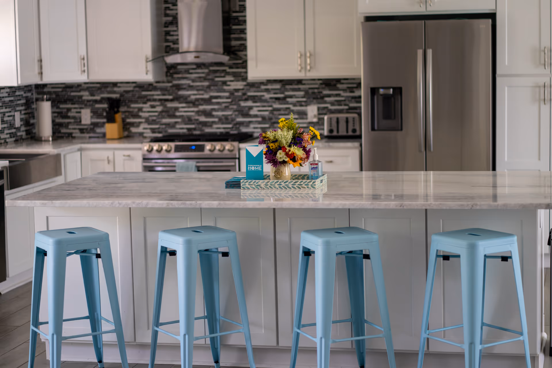 Bright modern kitchen with white cabinets, marble island, and light blue stools.