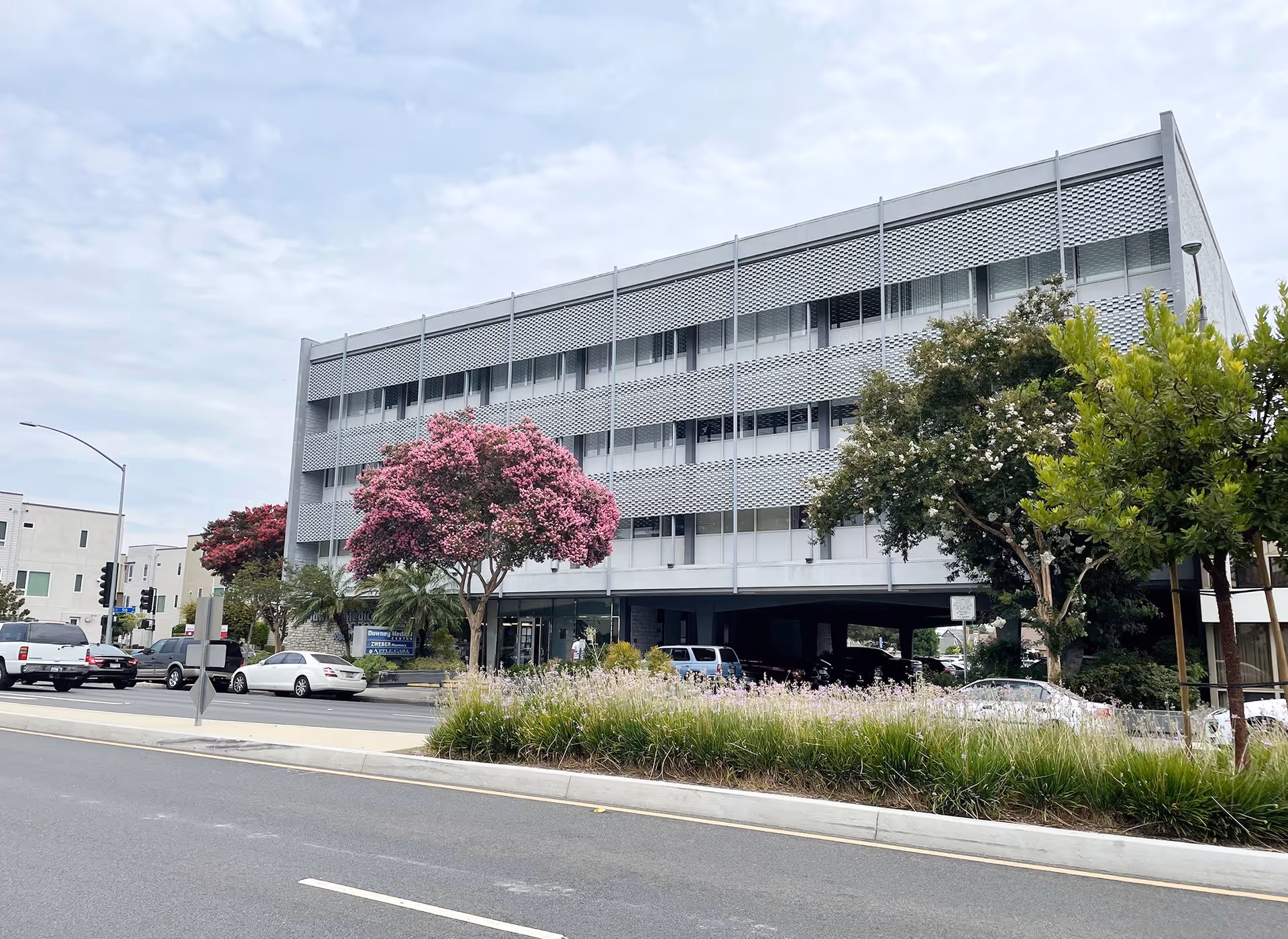 A modern, multi-story building along a tree-lined street with parked cars.