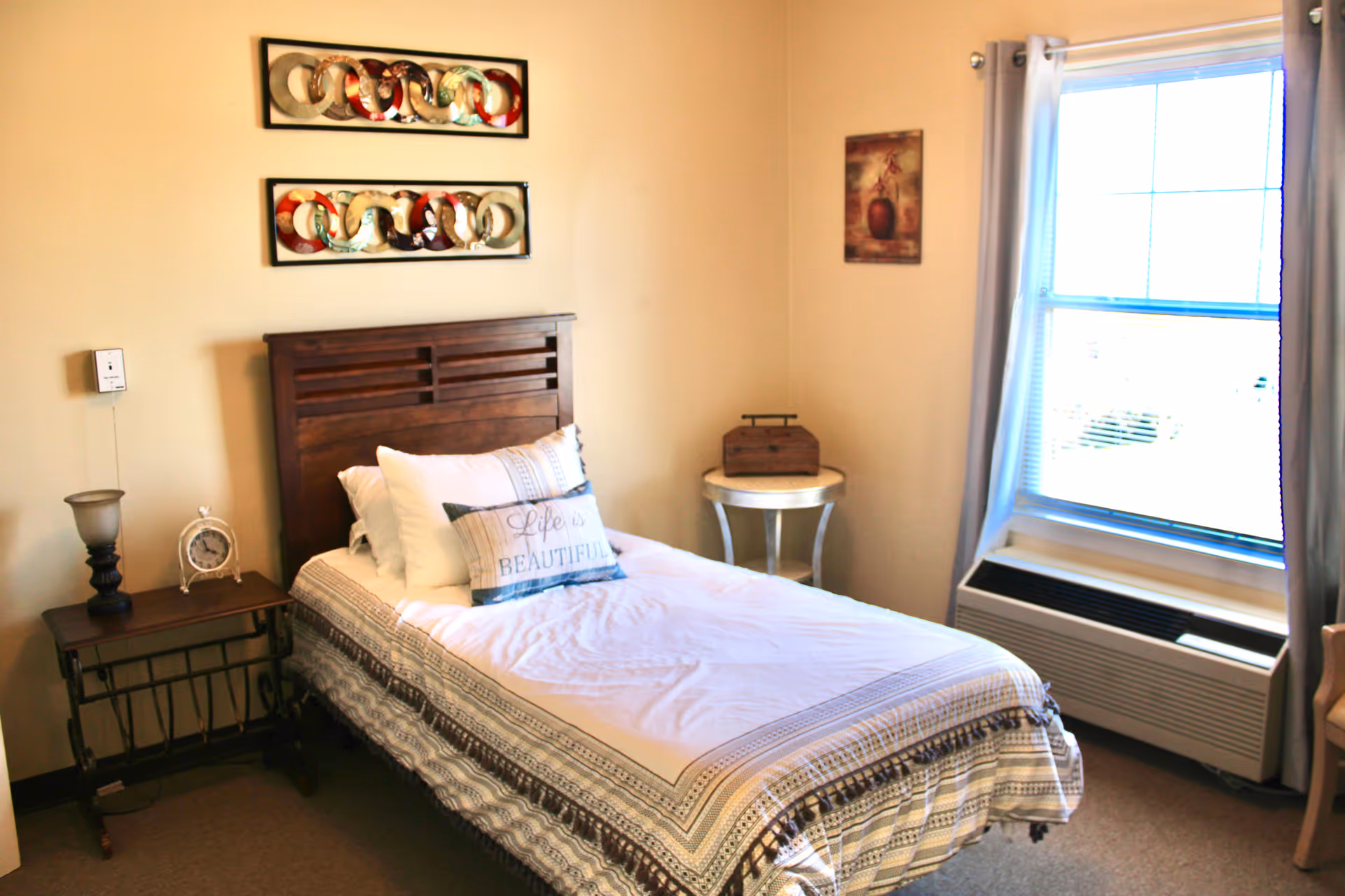 A cozy bedroom with a wooden bed, nightstand, wall art, and a window with curtains.