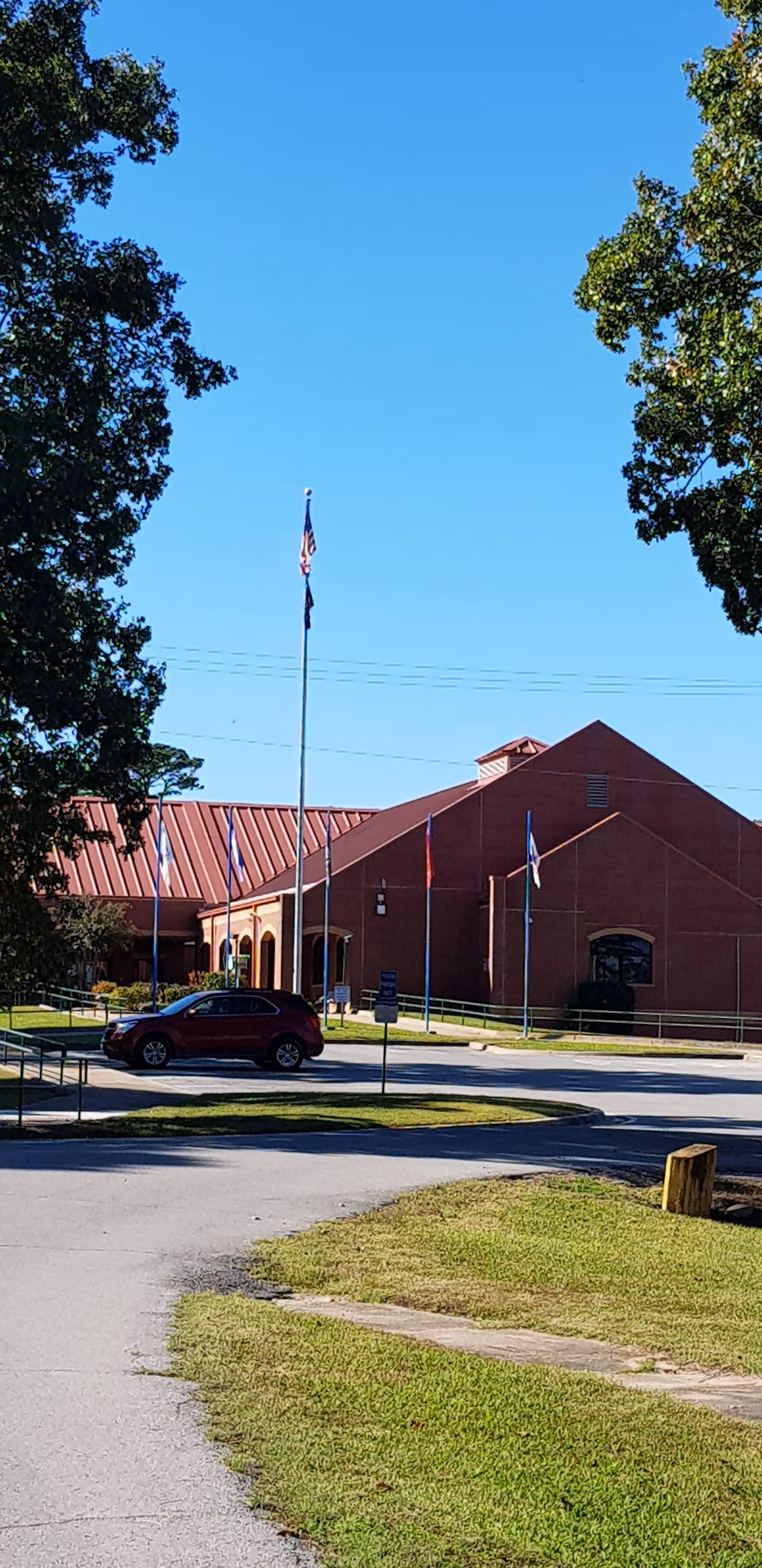 Front exterior of a brick senior living facility with flags, a parked car, and trees.