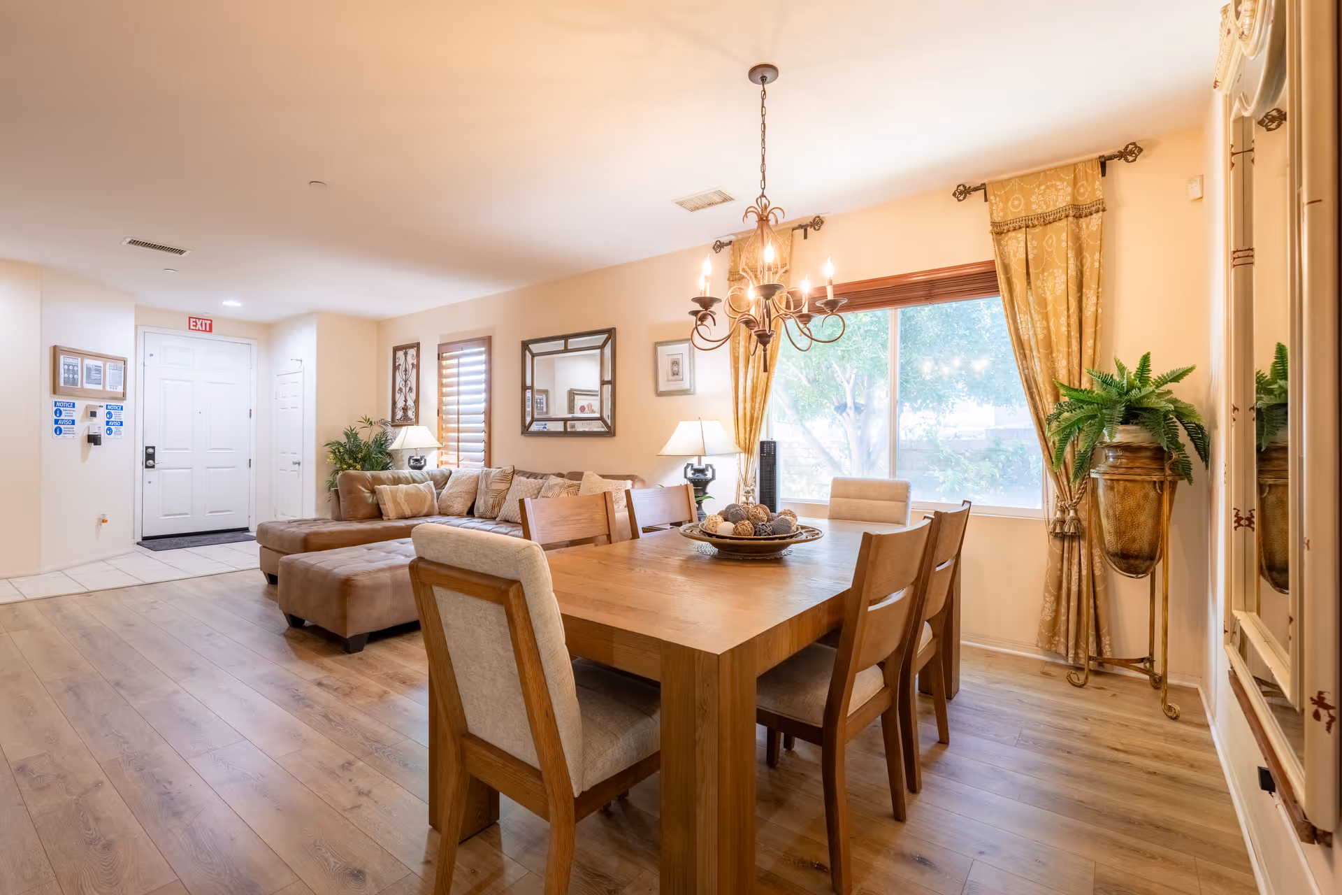 Bright dining room with wooden table, chairs, chandelier, and large window in a senior living space.