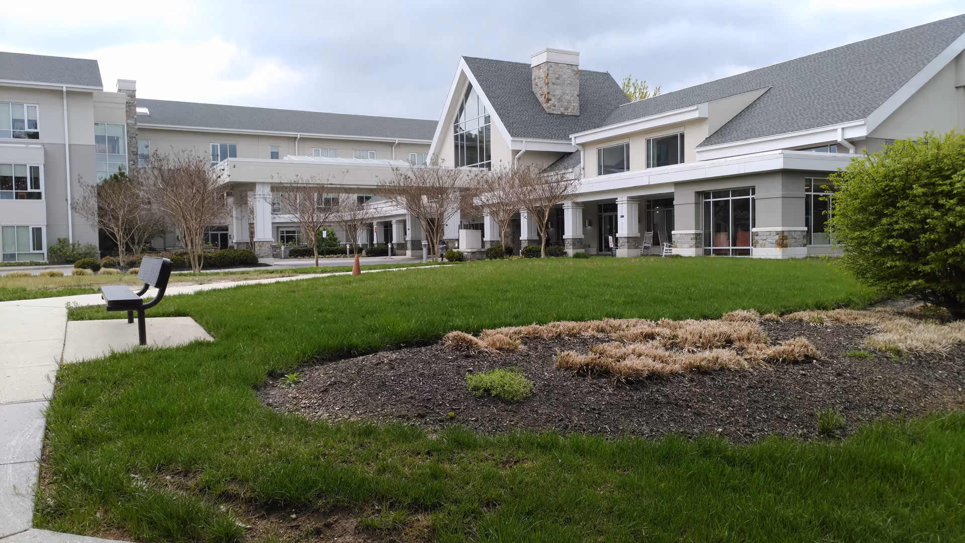 Exterior view of a modern senior living facility with green lawn, walkway, and benches.