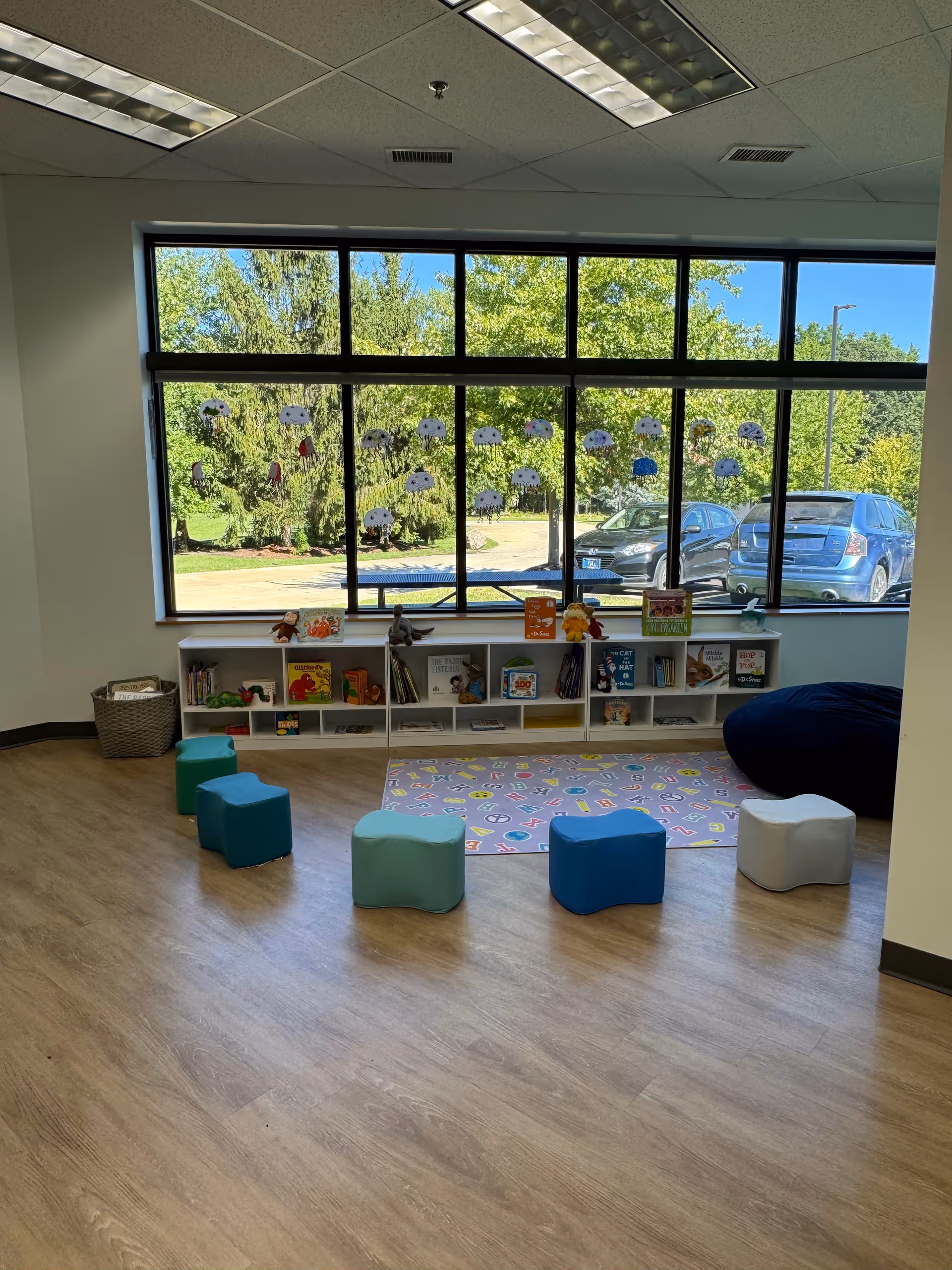 Bright playroom with shelves, cubbies, books, colorful stools, and large windows.