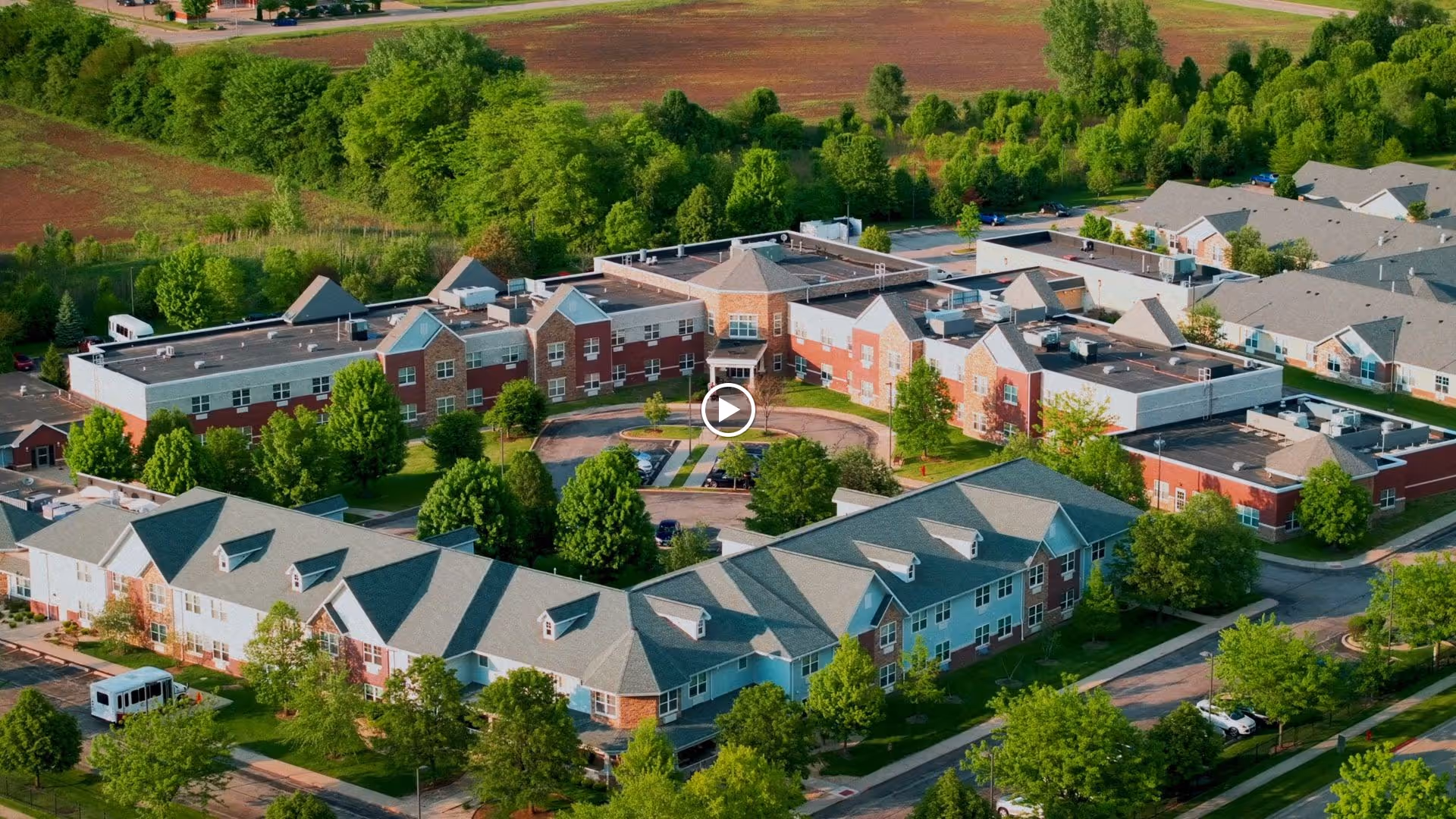 Aerial view of Serenity Estates of Morris, showing a large senior living facility with multiple connected buildings surrounded by trees and greenery, with parking areas and roads visible.