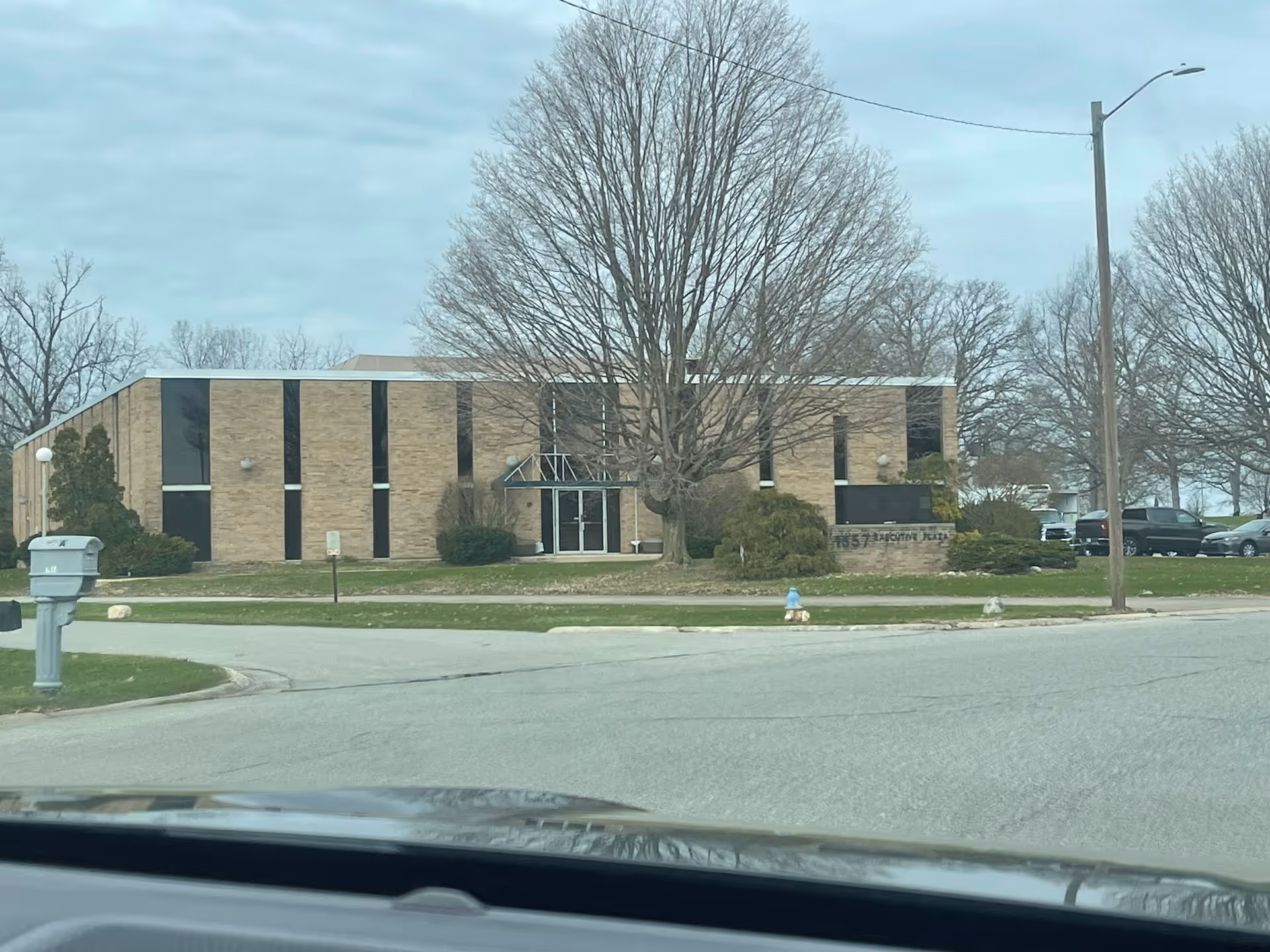 Exterior view of a brick senior care building with trees and driveway.