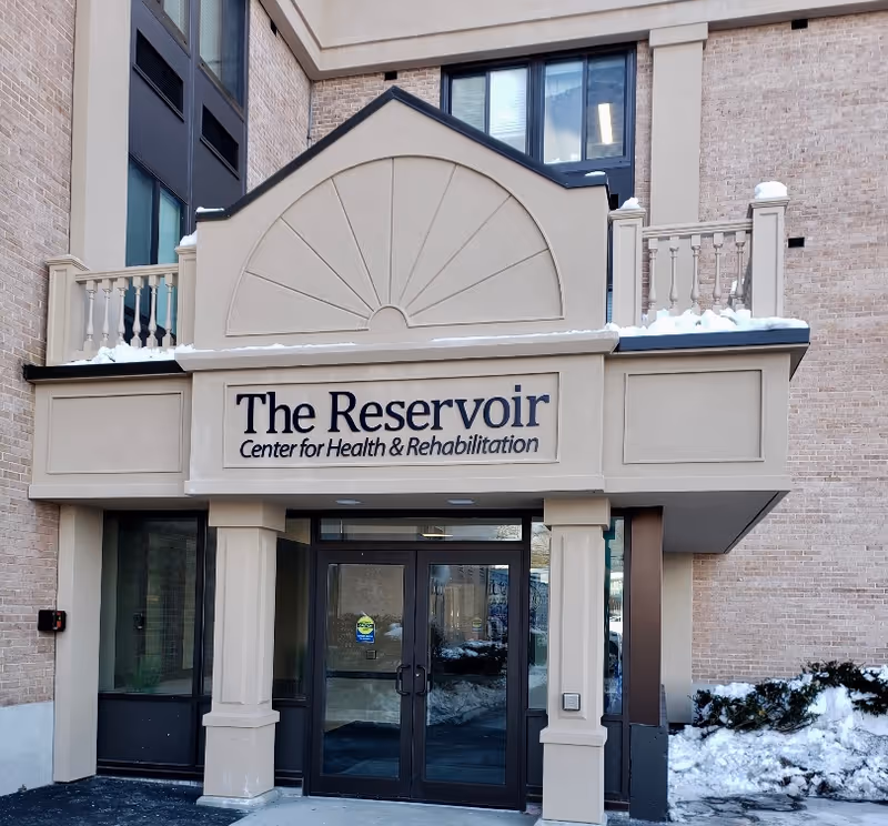 Exterior view of The Reservoir Center for Health and Rehabilitation entrance with sign and snow.