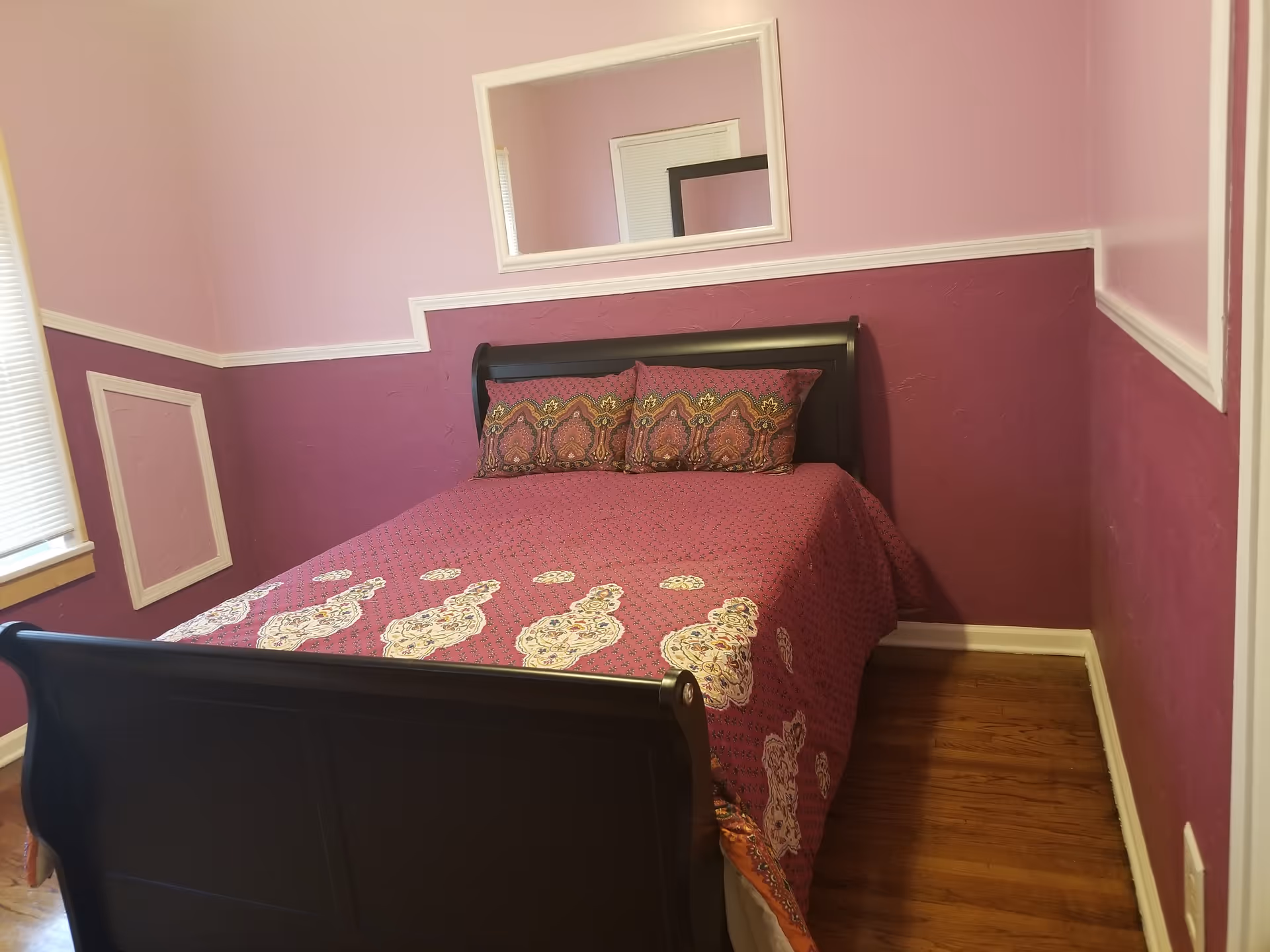 Cozy bedroom in a senior facility with purple walls, dark bed, and a wall mirror.