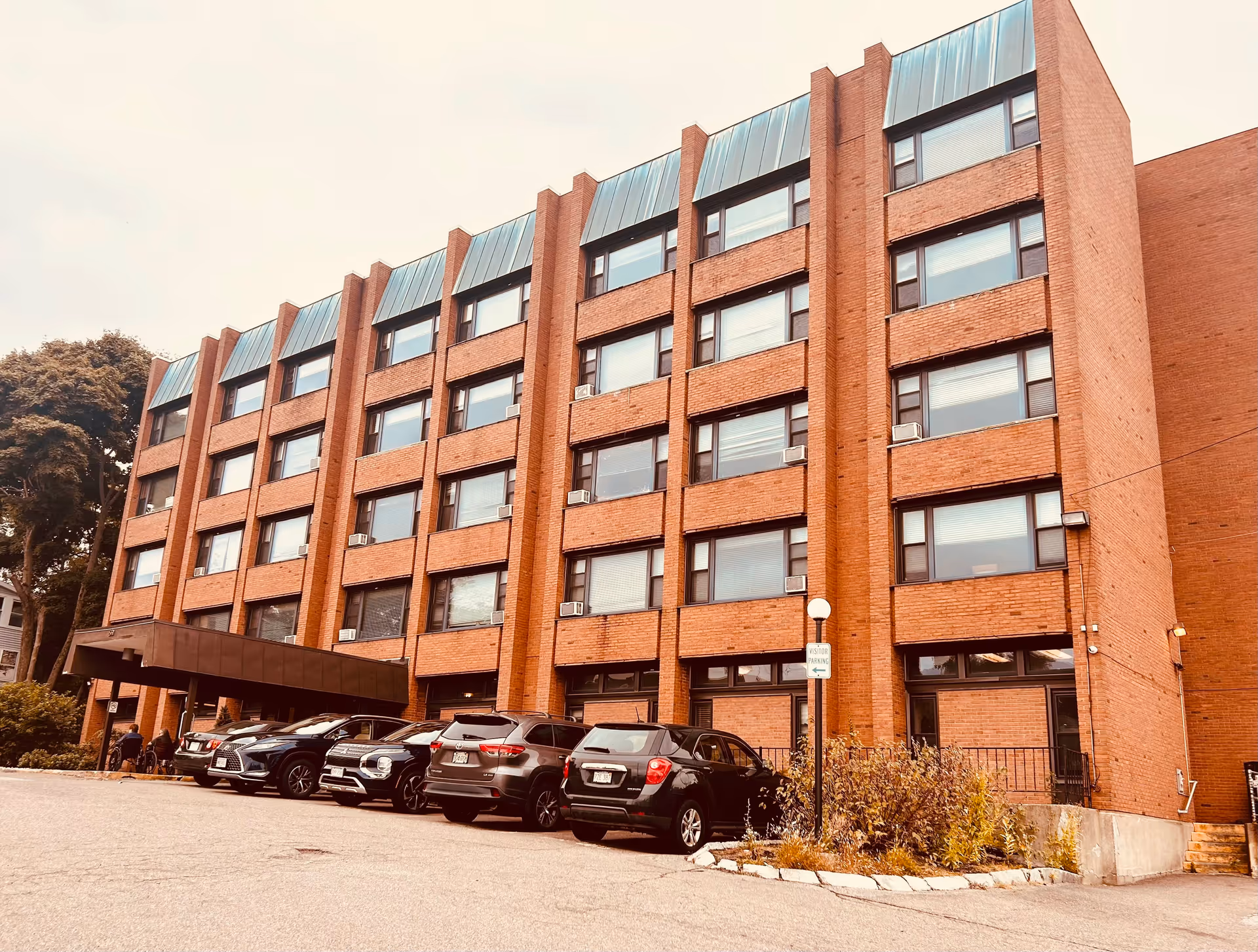 Brick multi-story health facility with a car-filled parking lot and covered entrance.