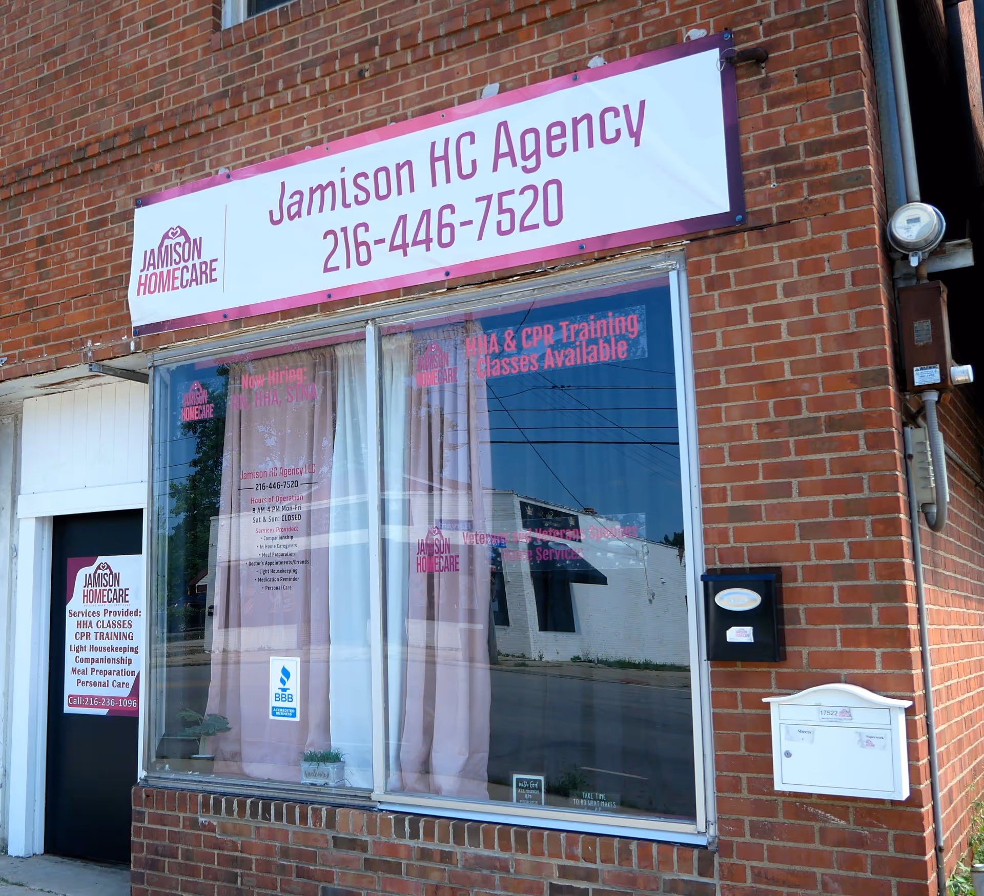 Brick building storefront with Jamison HC Agency sign and pink-curtained windows.