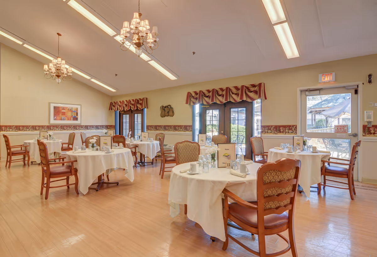 Senior living dining room with round tables, chairs, and chandeliers.