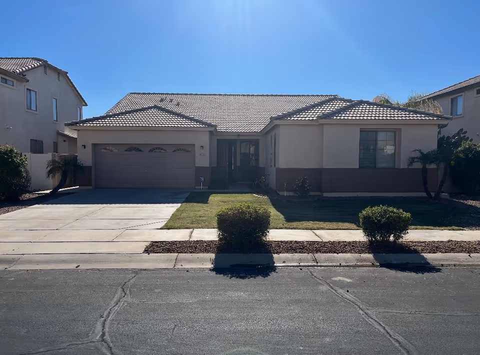 A single-story beige house with a two-car garage and front lawn under blue sky