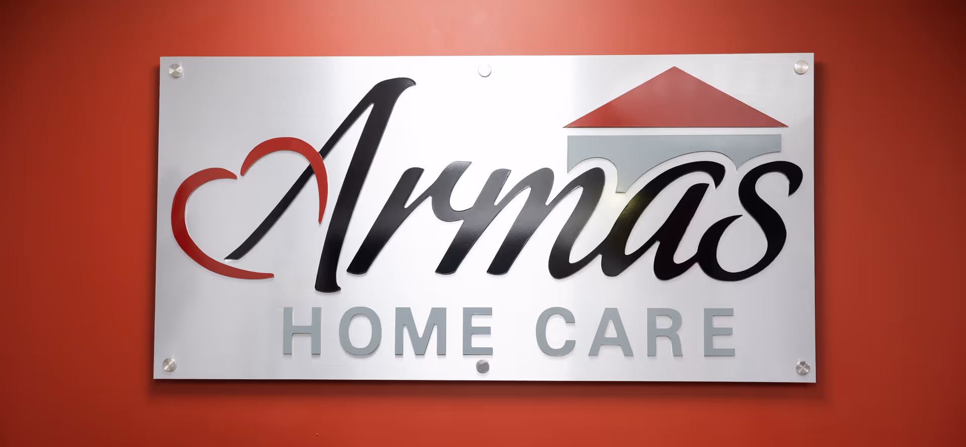 Metal sign reading Armas Home Care mounted on a red wall.
