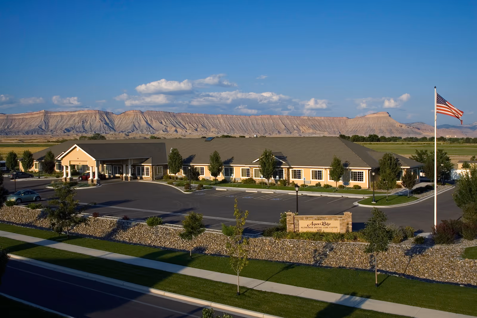 Aspen Ridge Alzheimer's Special Care Center exterior with parking, flagpole, and mountainous backdrop