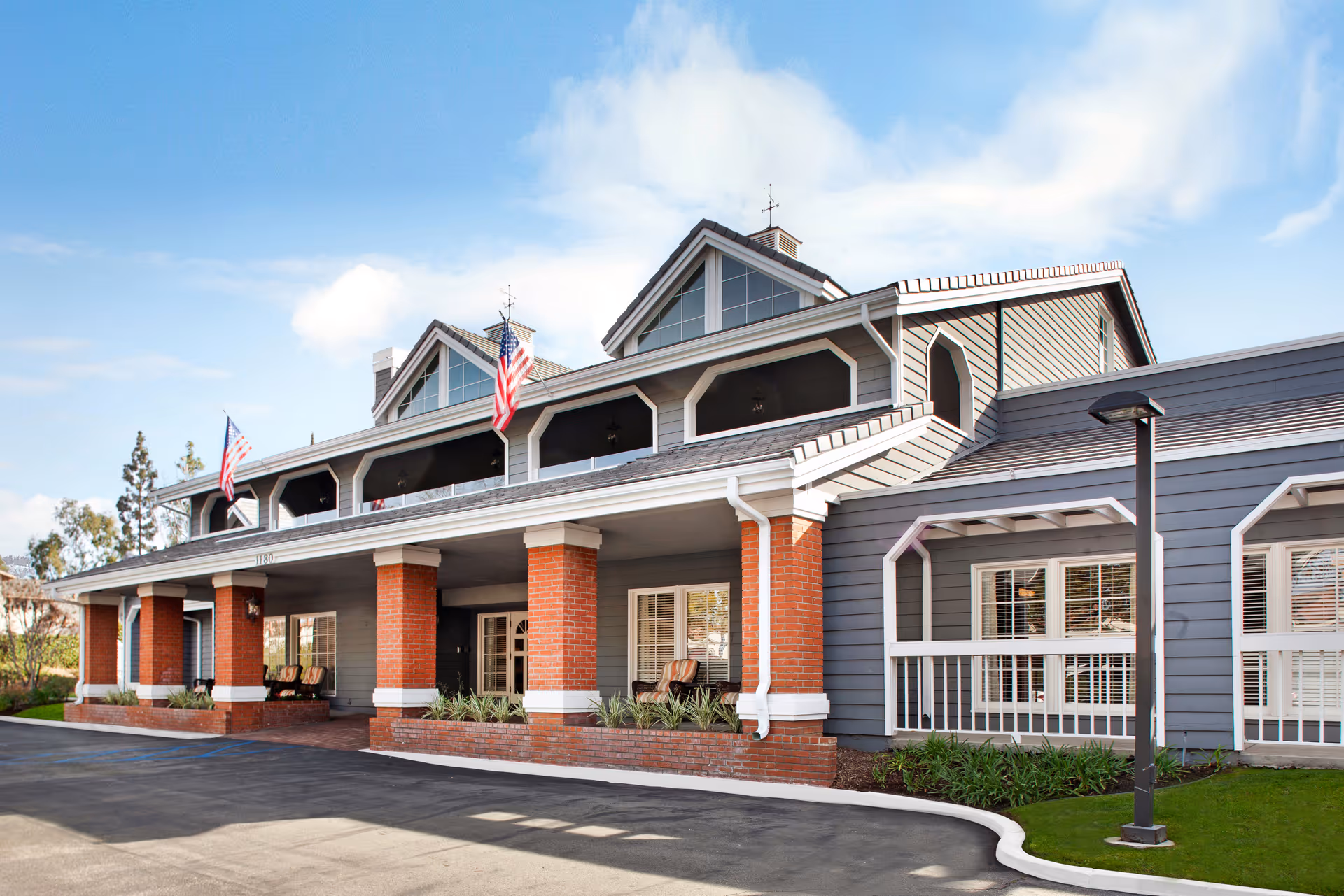 Senior living facility exterior with brick columns, blue siding, and flags at the entrance