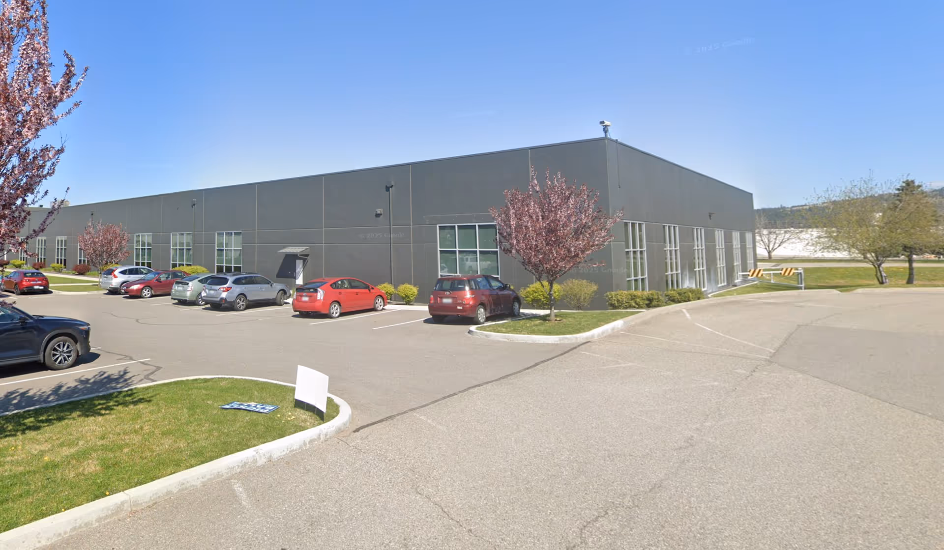 A large gray industrial-style building with a parking lot and blooming trees in front.
