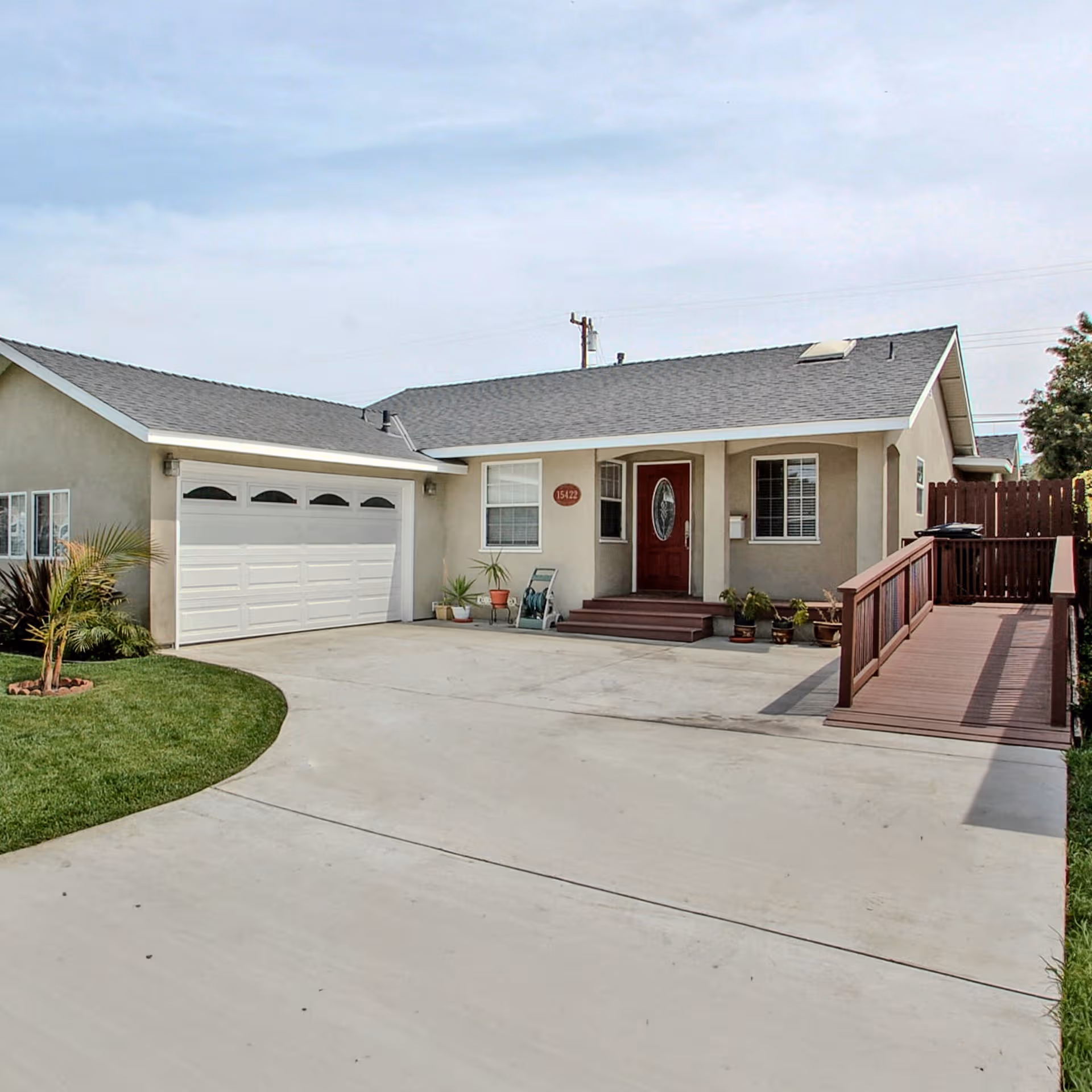 Single-story beige house with a two-car garage, front ramp, and potted plants at entrance.