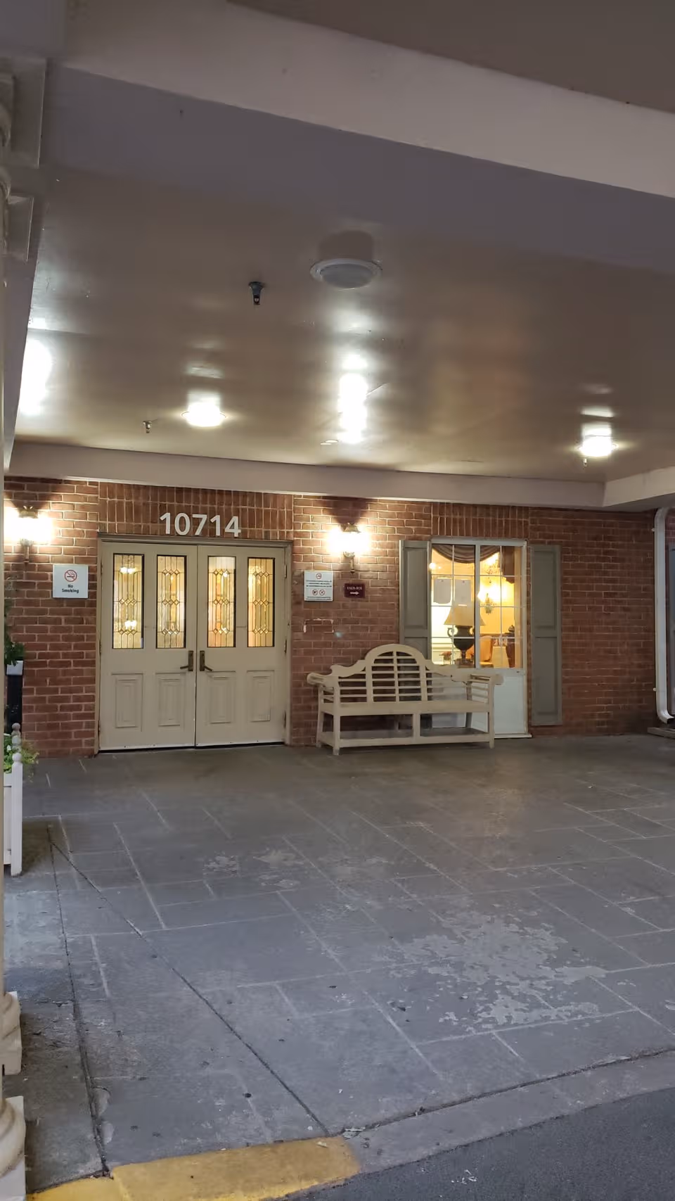 Exterior entrance of a brick senior living facility with a white bench