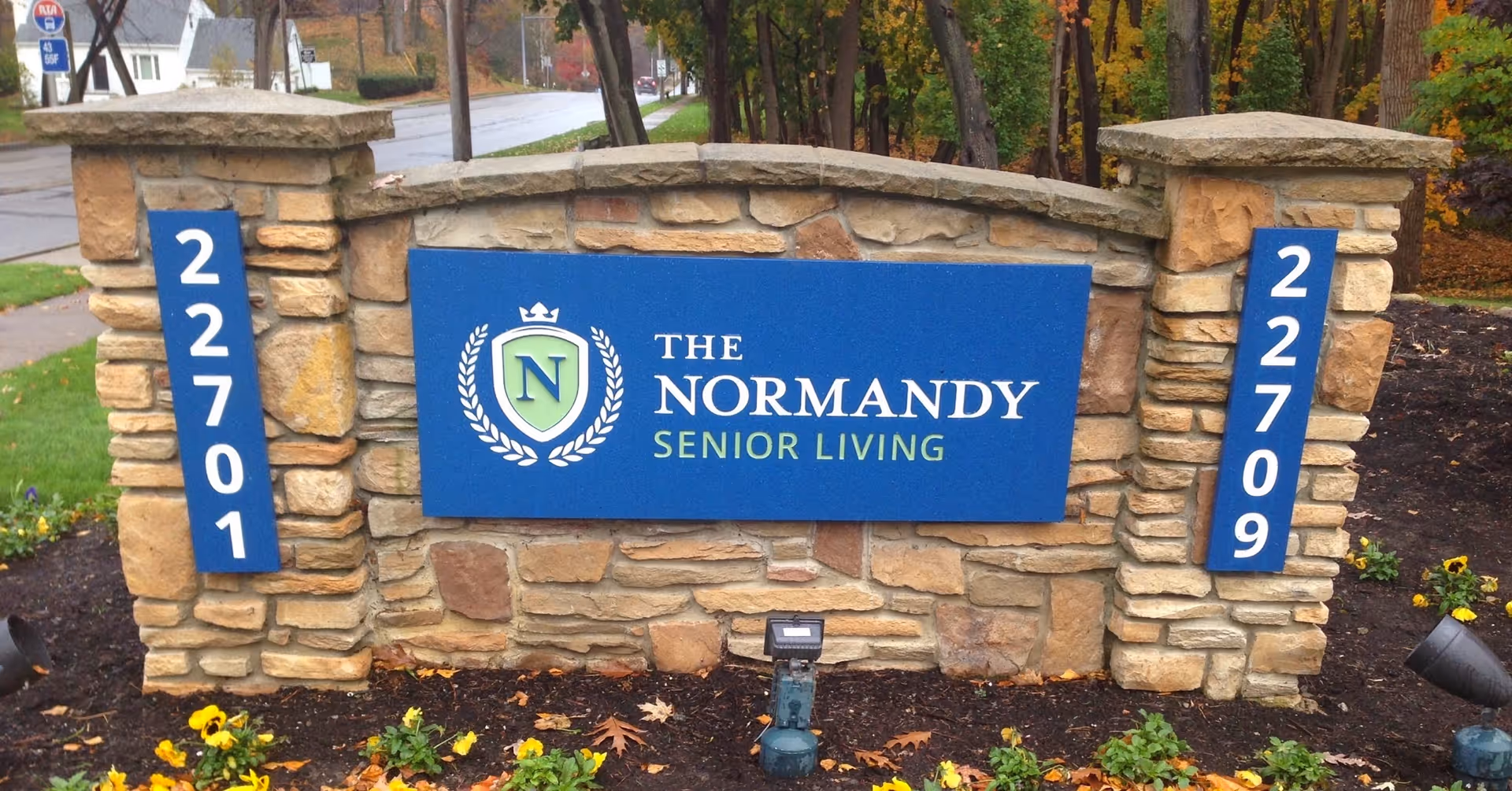 Stone entrance monument with blue sign reading The Normandy Senior Living.
