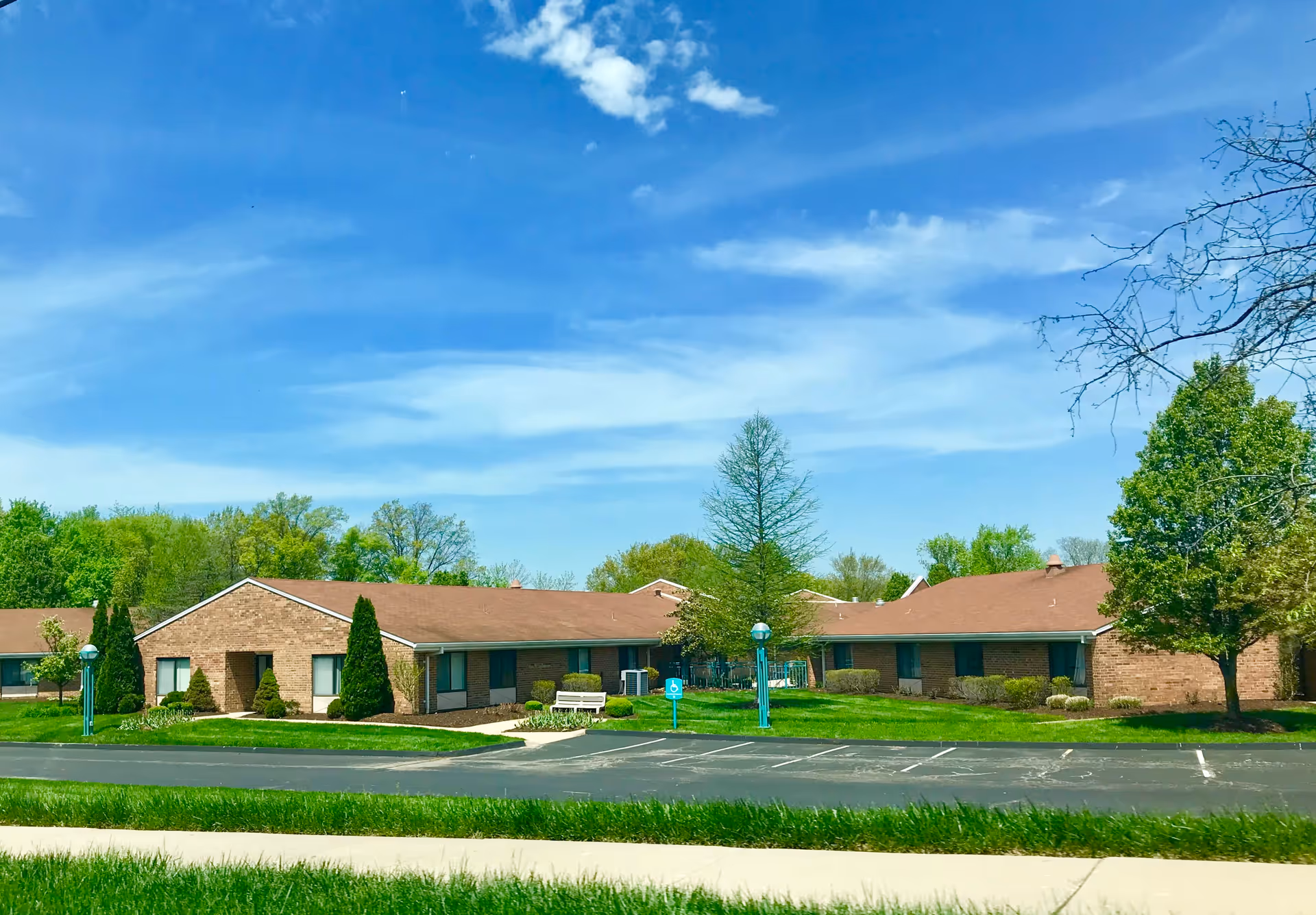 Exterior of a single-story brick senior living building with parking lot and green lawn.