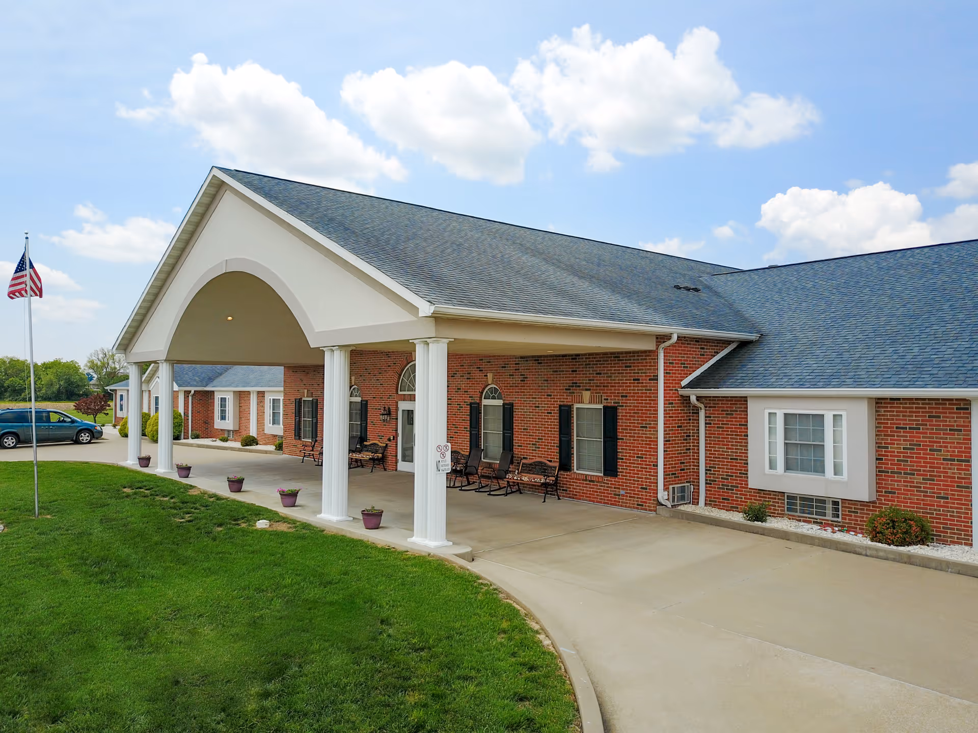 Brick senior living facility with a covered entrance, columns, and a well-kept front lawn.