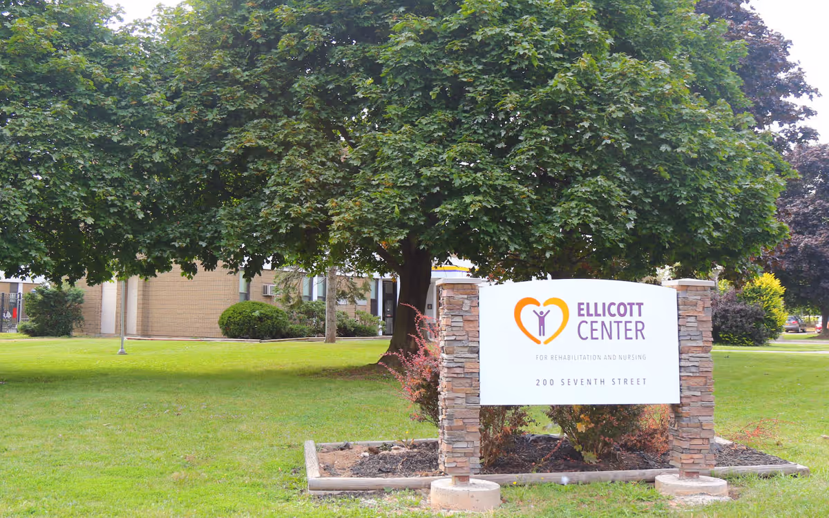 A large tree beside a sign that reads Ellicott Center, in front of a brick building.