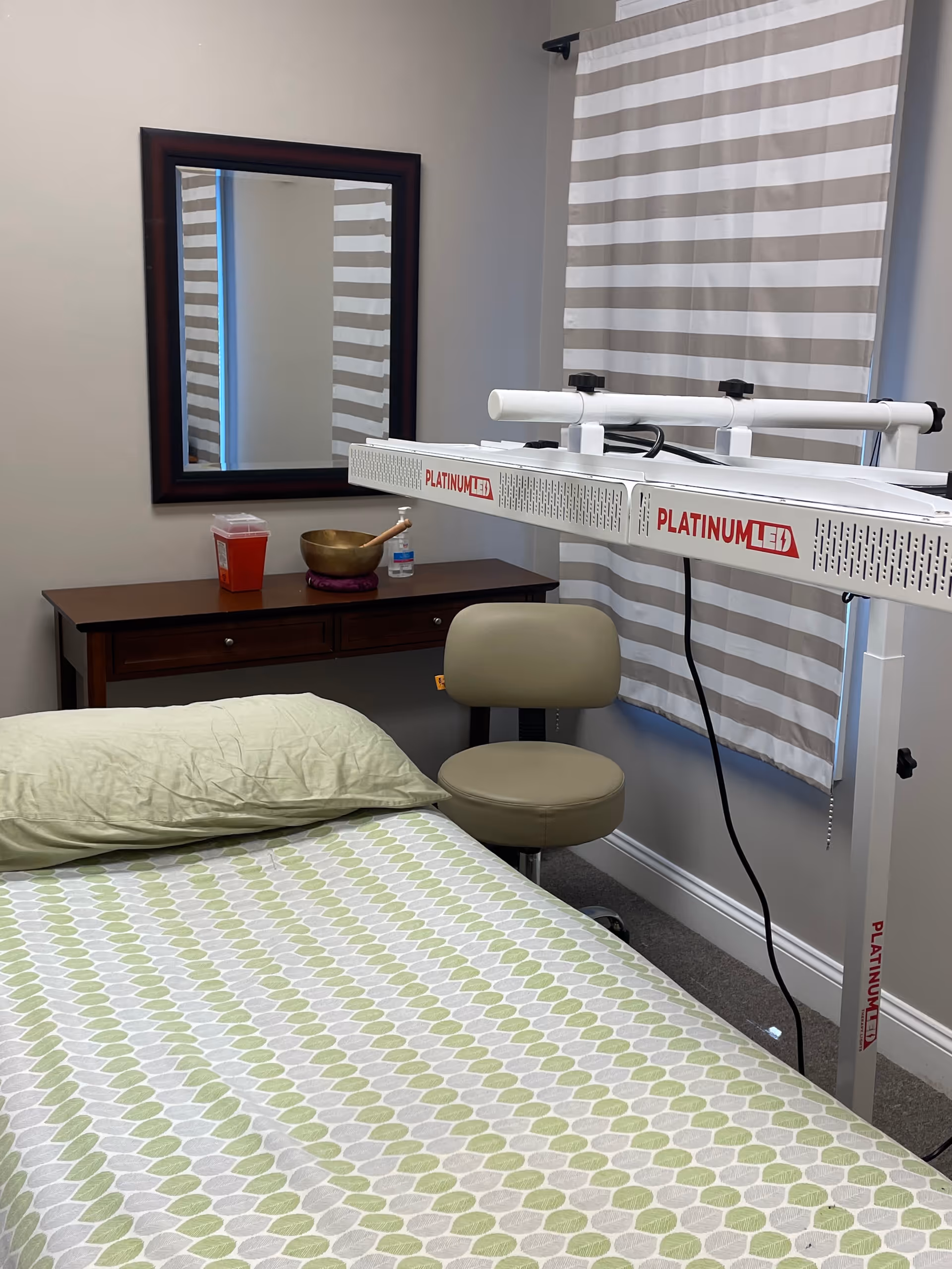 Treatment room with bed, chair, dresser, mirror, and PlatinumLED device.