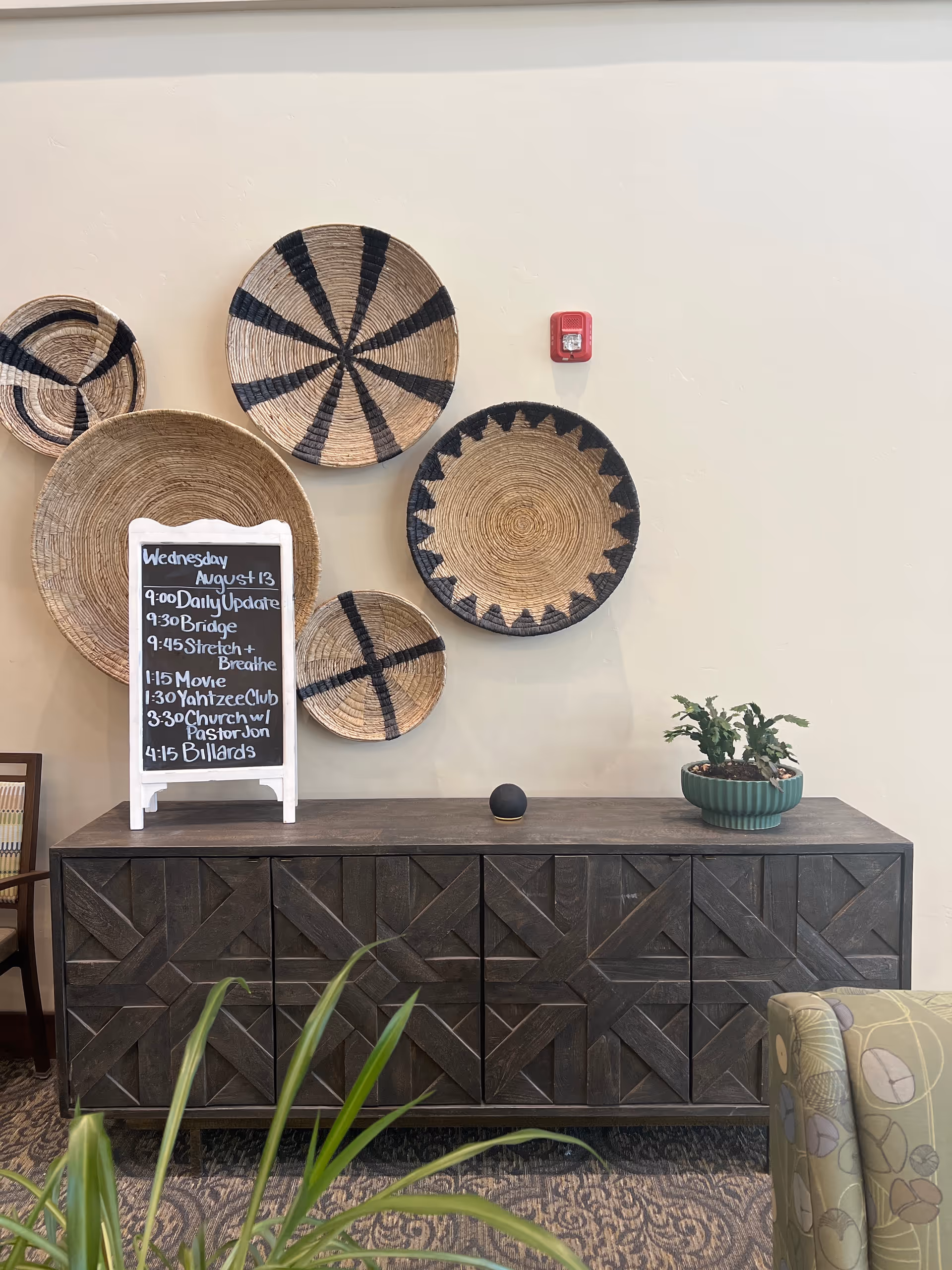 Interior common area with woven baskets on wall, chalkboard, plant, and dark cabinet.