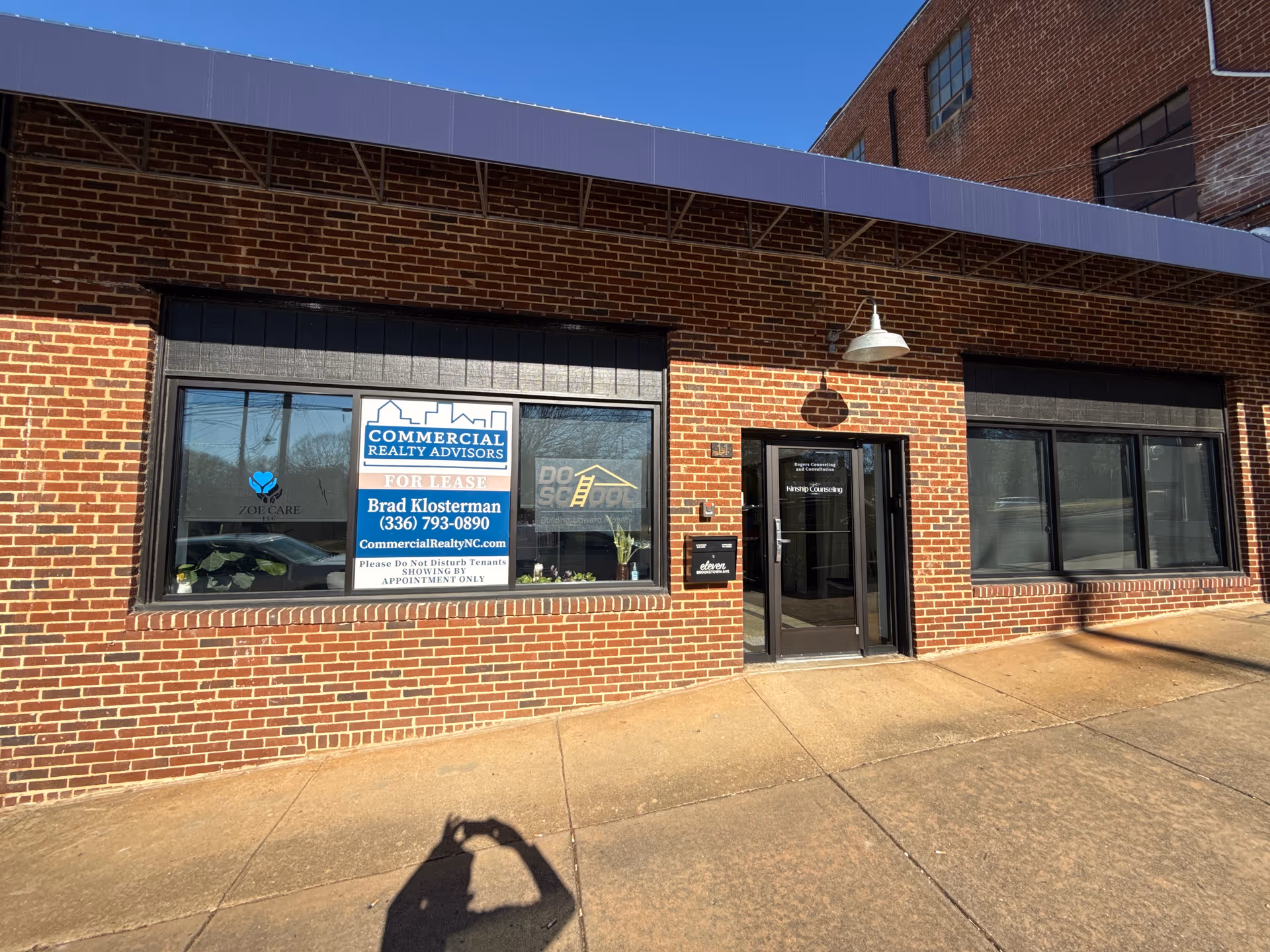 Brick storefront with large windows, a glass door, and a 'FOR LEASE' sign.