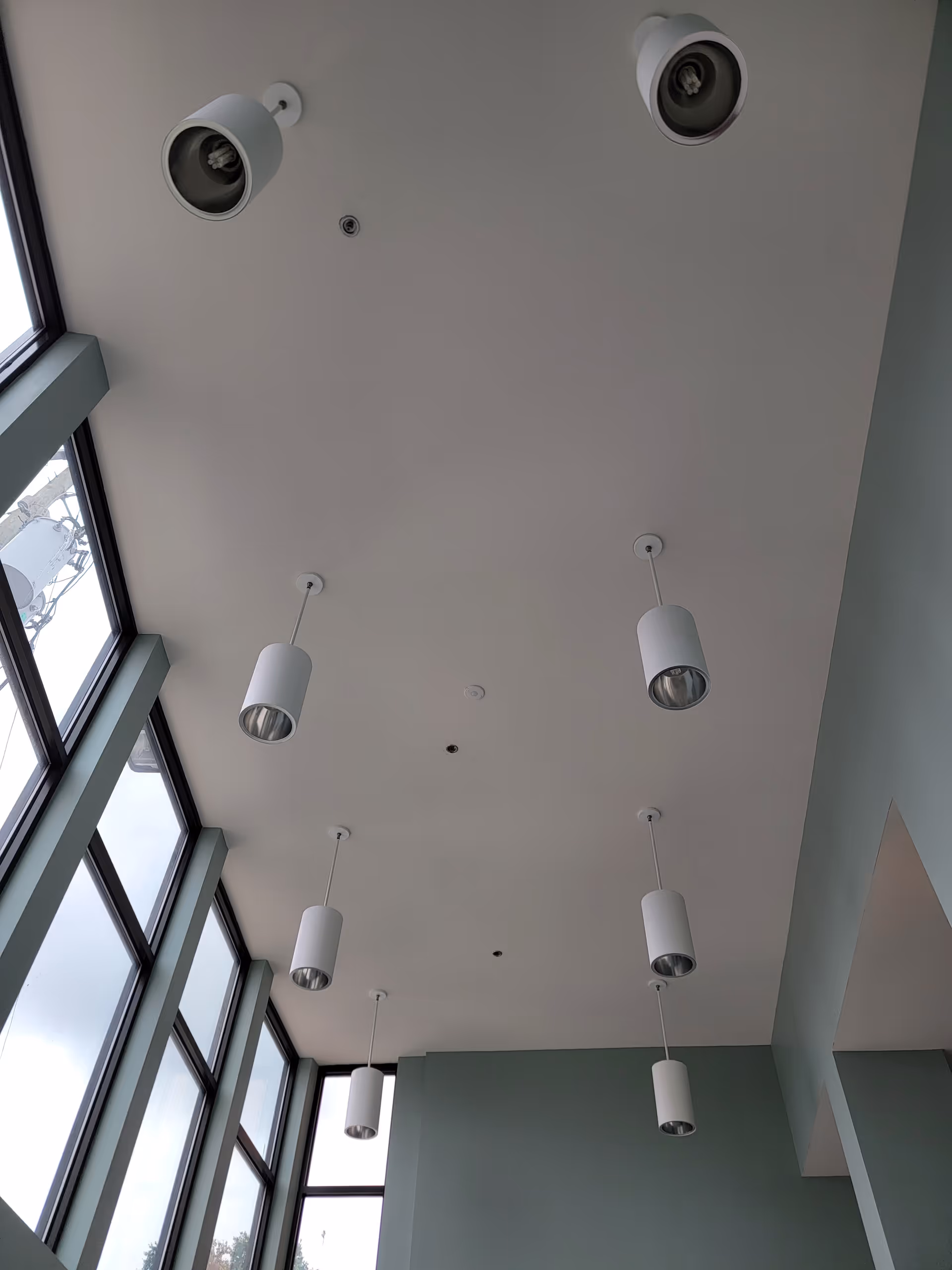 Interior ceiling with white pendant lights and tall windows along the left wall.