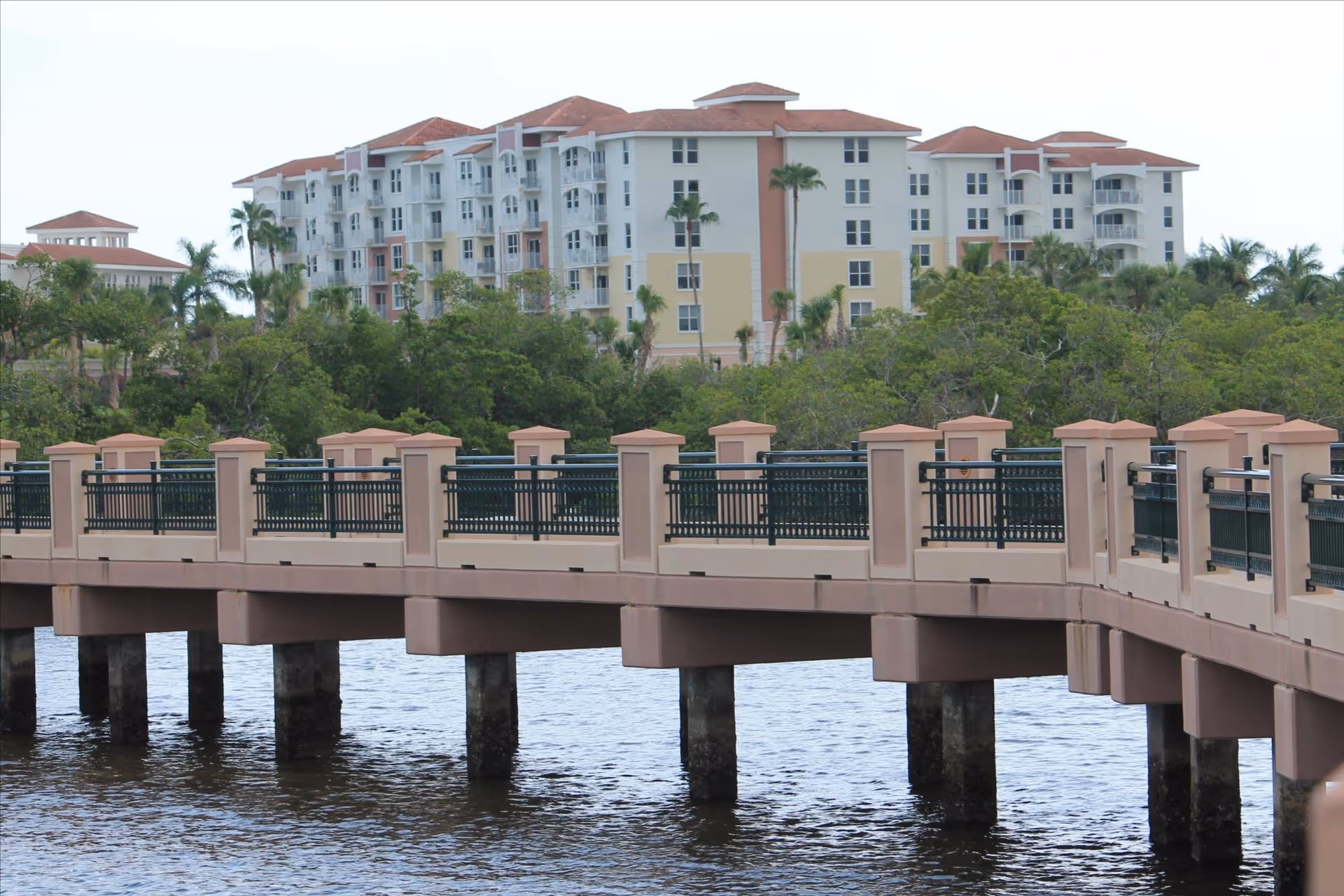 A large multi-story senior living building sits behind a pink bridge over water.