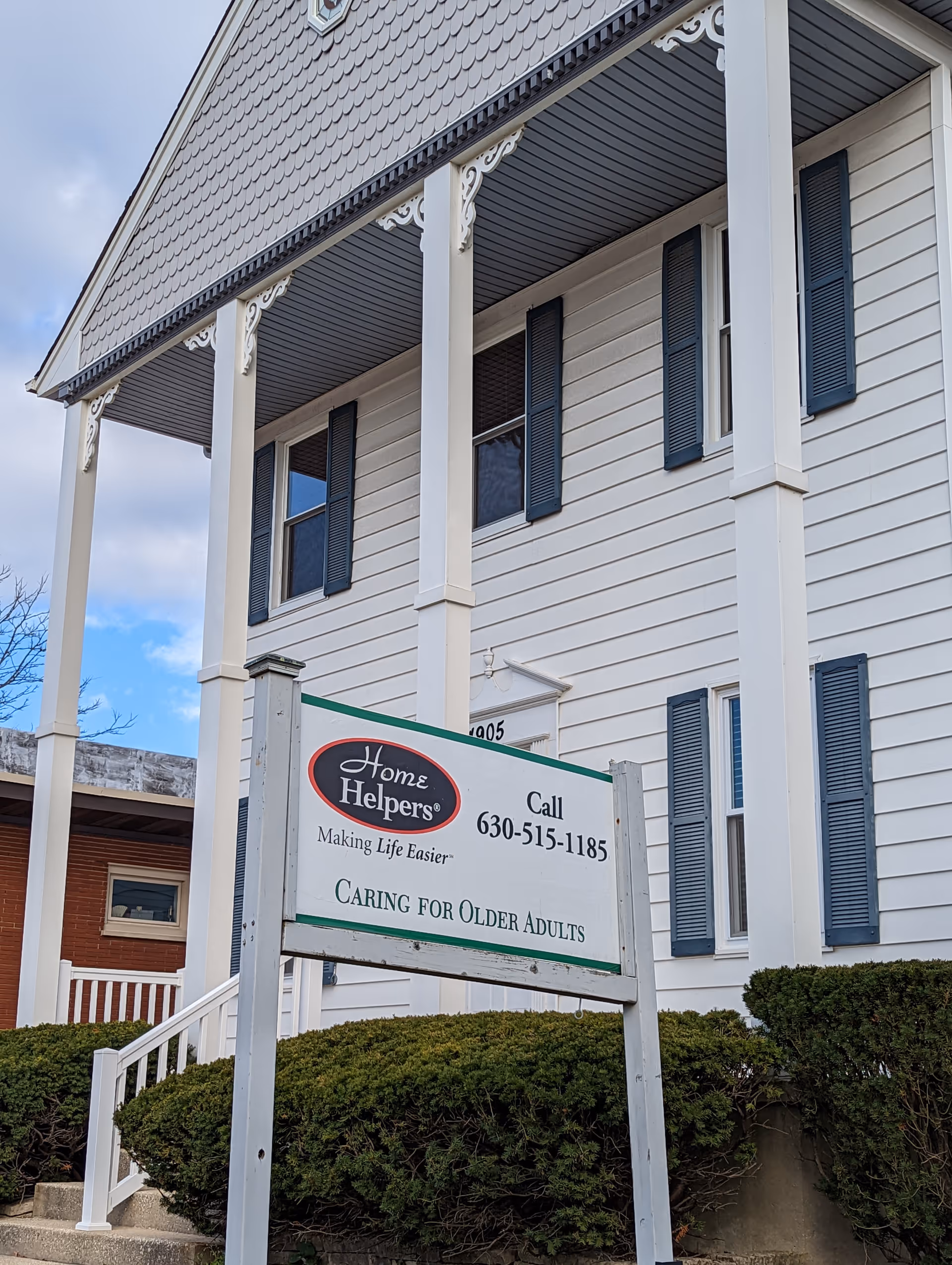 White two-story building with decorative porch columns and a Home Helpers sign.