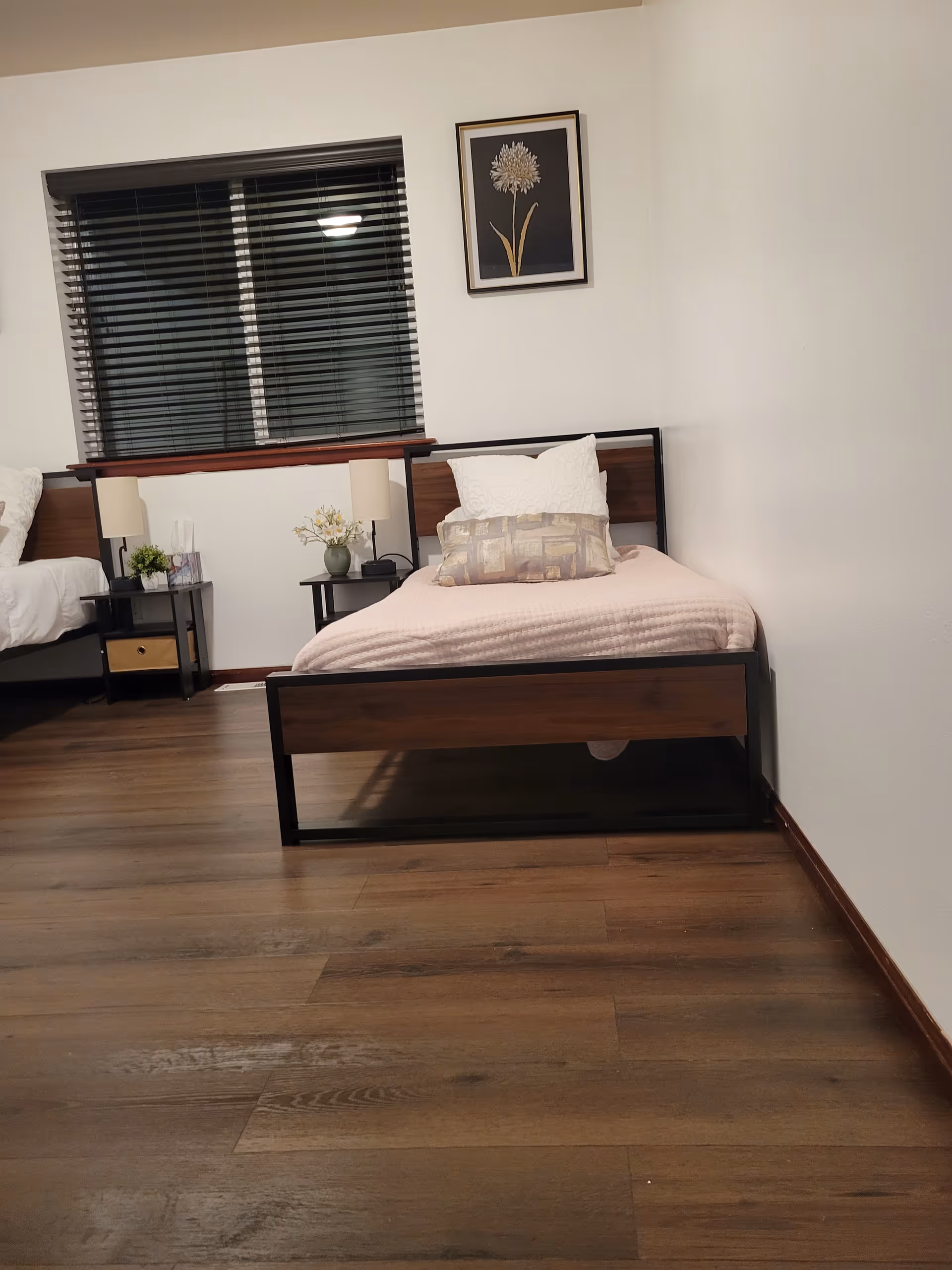 A clean bedroom with two beds, nightstands, lamps, and a framed flower picture.