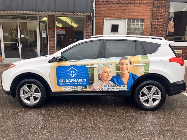 White SUV parked outside a building with a blue St. Raphael's Home Care advertisement.