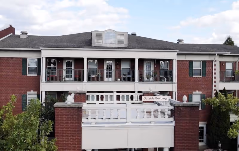 Exterior view of a brick senior living building with balconies and greenery.