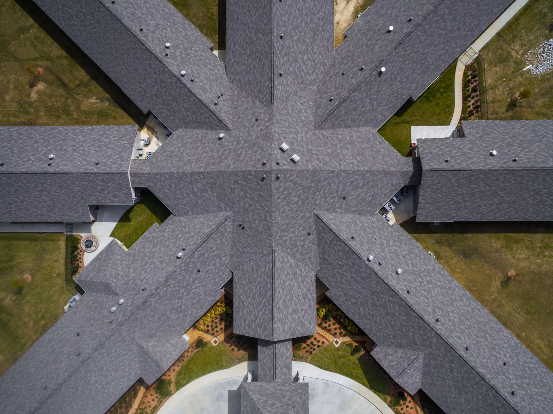 Aerial top-down view of a cross-shaped building roof with surrounding walkways and lawns.