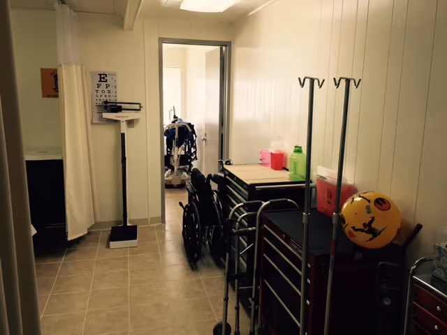 Narrow interior hallway with medical carts, wheelchairs, and IV stands.