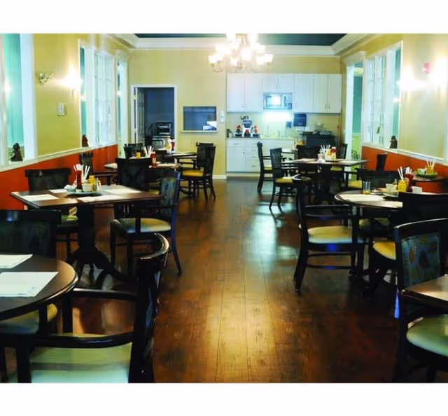 Spacious dining room with round tables, chairs, and a serving counter at the back.