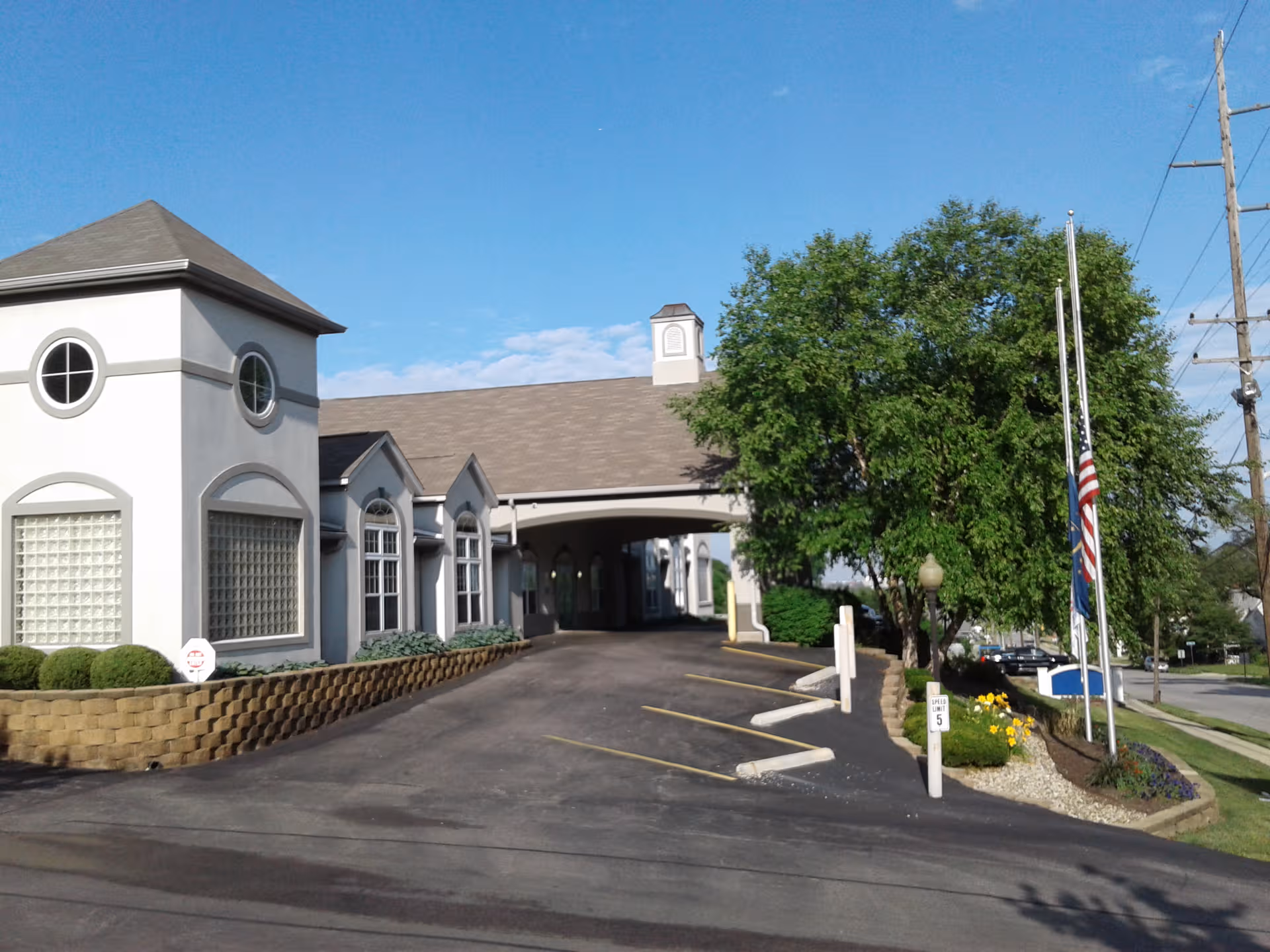 Exterior view of Rosewalk Village entrance with drive, greenery, and flags.