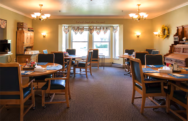 An empty Cantril House Assisted Living dining room with round tables, chairs, and large windows.